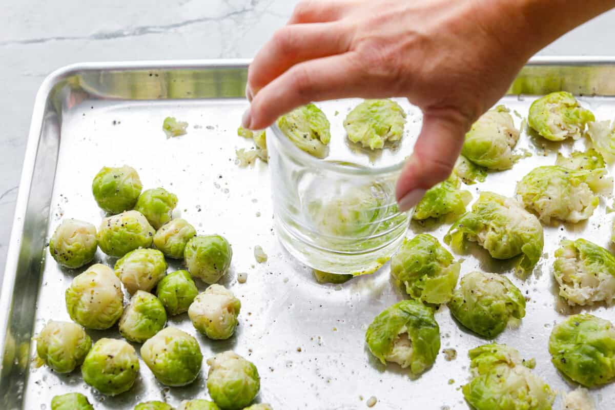 Irresistibly crispy Smashed Brussels Sprouts areย simple to make, loaded with delicious flavor, and have the best crunchy texture. These pair well with almost any protein and will definitely upgrade your side dish game! Angle shot of someone smashing boiled, oiled, and seasoned Brussels sprouts.