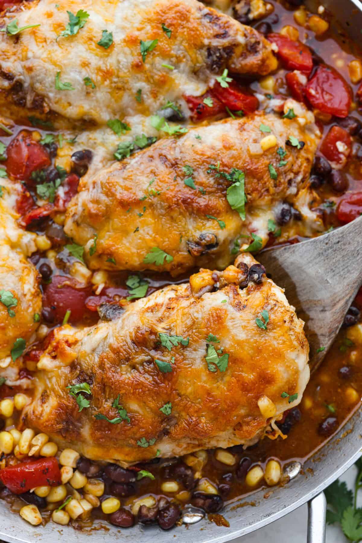 This cowboy chicken recipe is packed with bold flavors. The chicken is seared with lots of vibrant seasonings, surrounded by corn, black beans, and fire-roasted tomatoes, all smothered in melty cheese. Your family will love this quick meal that is ready in just 35 minutes! Close up shot of cooked cowboy chicken.