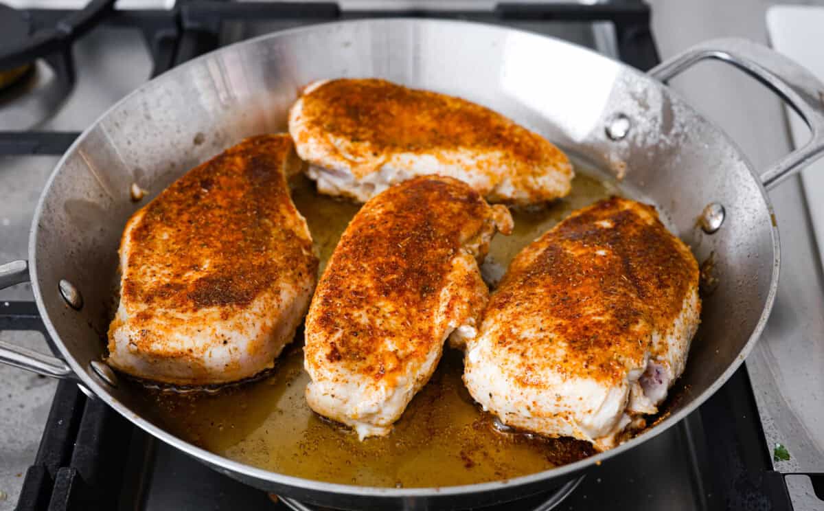 This cowboy chicken recipe is packed with bold flavors. The chicken is seared with lots of vibrant seasonings, surrounded by corn, black beans, and fire-roasted tomatoes, all smothered in melty cheese. Your family will love this quick meal that is ready in just 35 minutes! Angle shot of the chicken being seared in a pan.