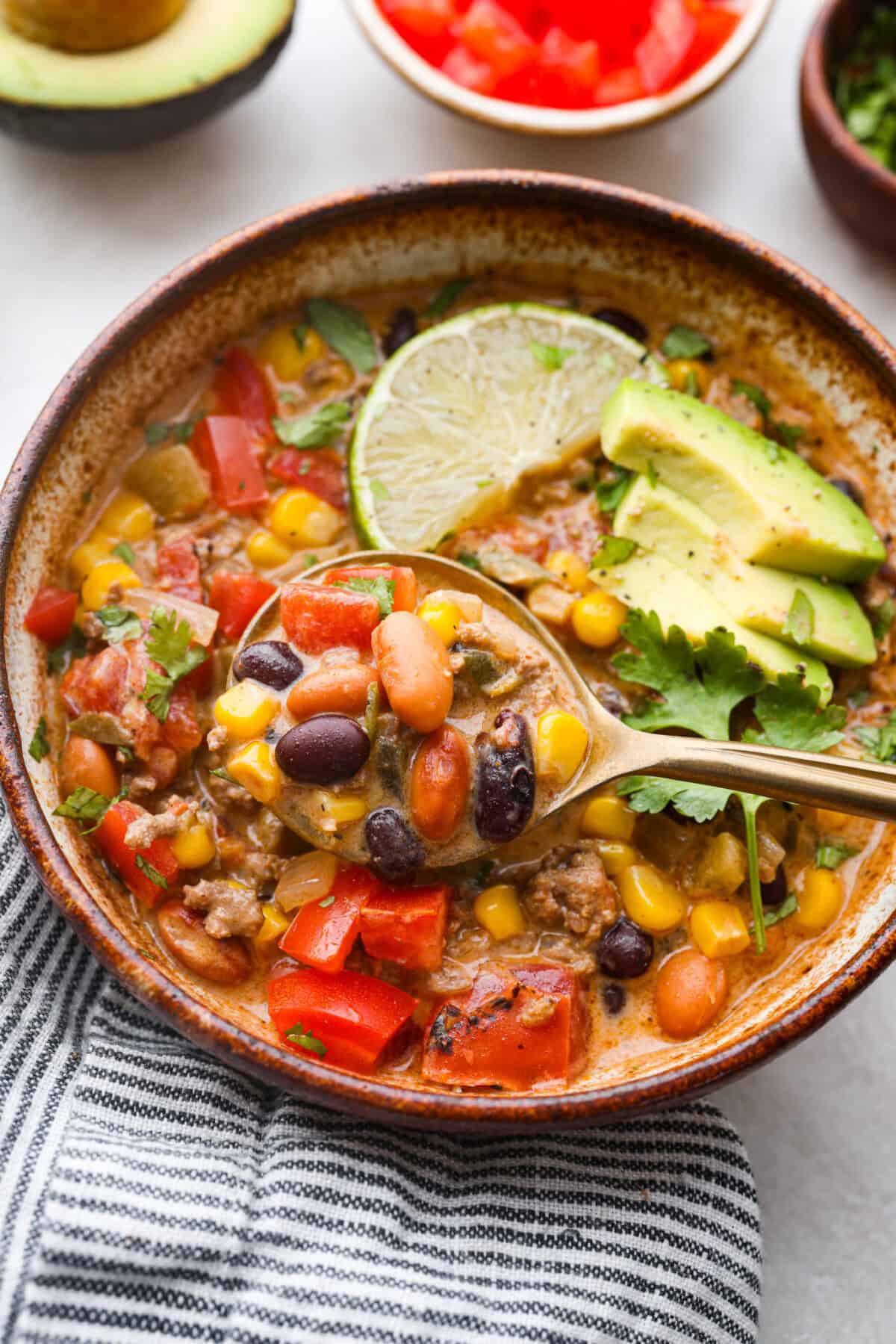 This creamy taco soup recipe is full of fresh flavors, tender vegetables, and hearty beans. The seasoned beef mixed with the creamy soup is out of this world good! Top it with your favorite toppings, and your family will love this warm, savory soup! Overhead shot of a bowl of creamy taco soup with a golden spoon scooping out a bite.