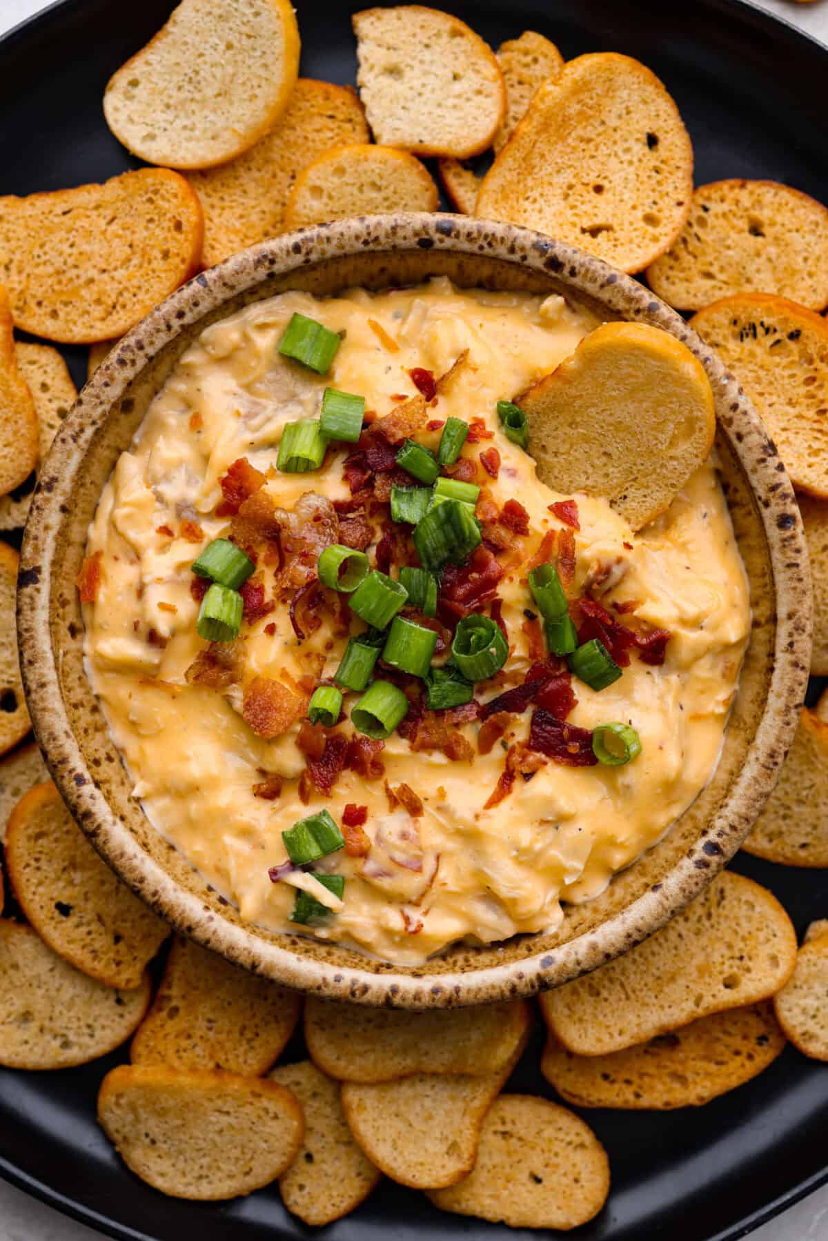 Get ready to be obsessed with this slow cooker crack chicken dip! The combination of chicken, cream cheese, Velveeta, bacon, and ranch seasoning creates an addicting snack that's perfect for holiday gatherings, game days, and parties! Overhead shot of slow cooker crack chicken dip in a bowl surrounded by toasted baguette pieces.