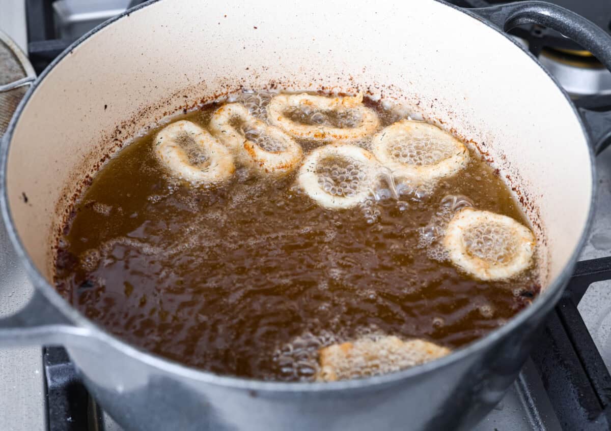 Crispy, flavorful Fried Calamari is a delicious appetizer that tastes like something you would order in a fancy restaurant. The calamari is tenderized, breaded and then fried to golden brown, crunchy perfection. Take it to the next level with marinara sauce for dipping! Angle shot of calamari being fried in a pot of oil.