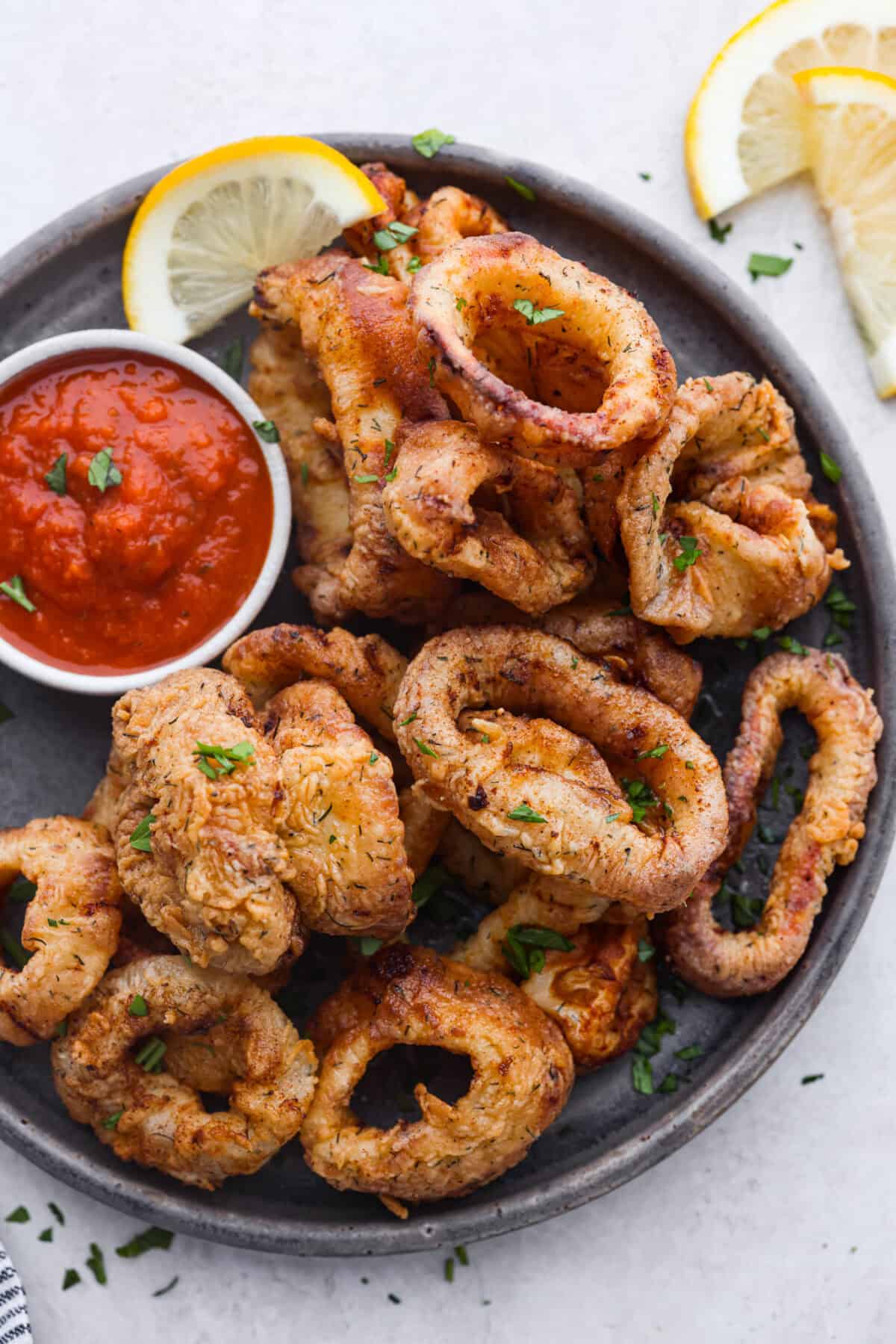 Crispy, flavorful Fried Calamari is a delicious appetizer that tastes like something you would order in a fancy restaurant. The calamari is tenderized, breaded and then fried to golden brown, crunchy perfection. Take it to the next level with marinara sauce for dipping! Overhead shot of fried calamari on a plate.