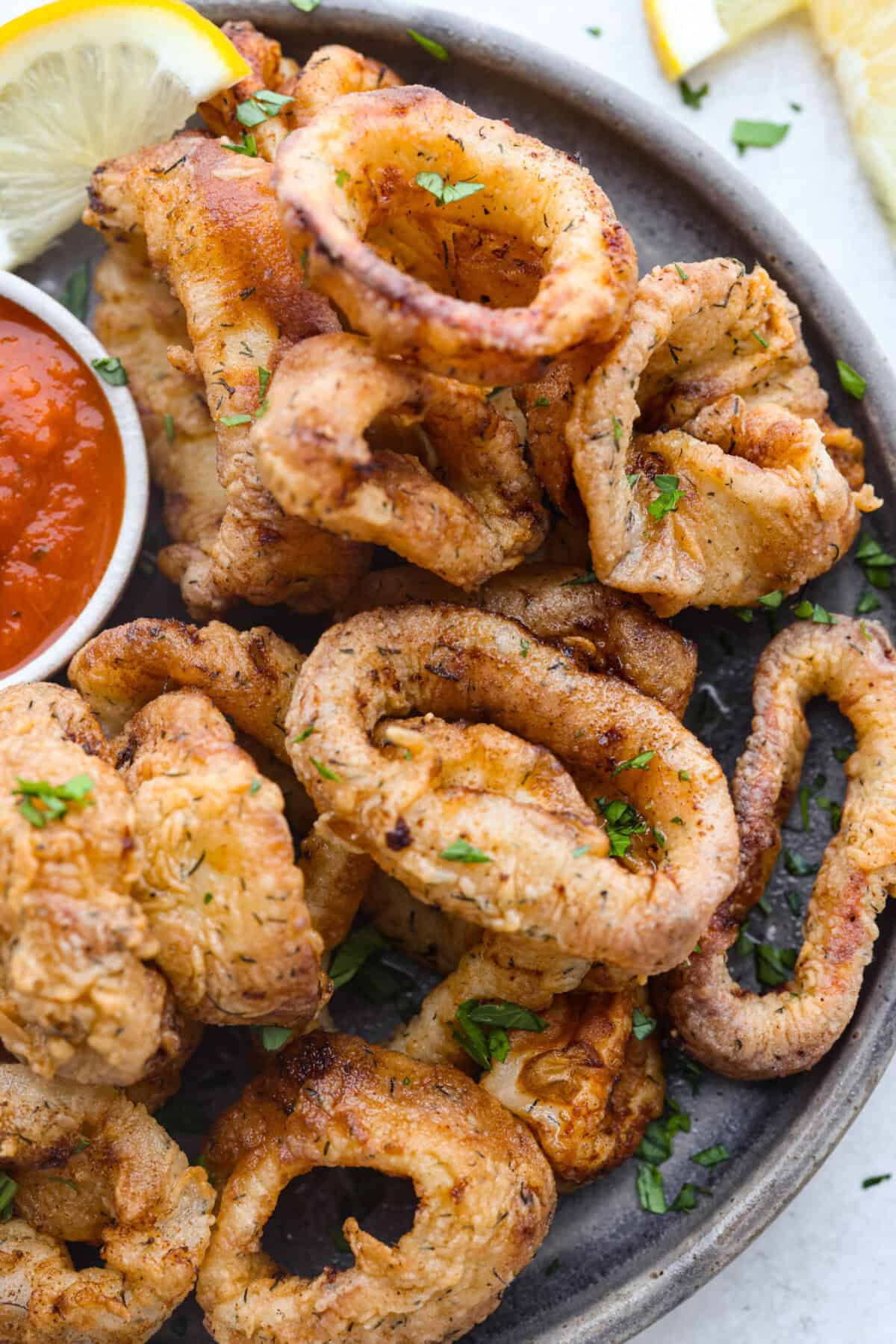 Crispy, flavorful Fried Calamari is a delicious appetizer that tastes like something you would order in a fancy restaurant. The calamari is tenderized, breaded and then fried to golden brown, crunchy perfection. Take it to the next level with marinara sauce for dipping! Overhead shot of plated calamari with marinara sauce on the side.