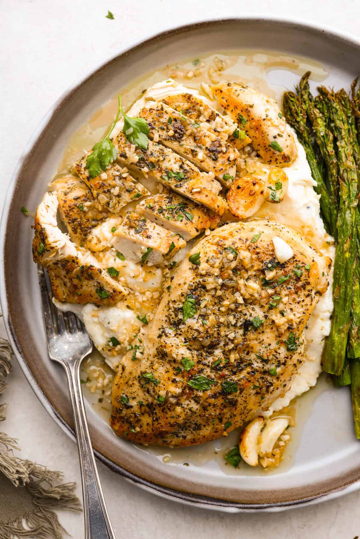 Garlic Butter Chicken is a rich and flavorful one-pan recipe that's on the dinner table in just 30 minutes! Well-seasoned, tender chicken breasts are pan-seared and then nestled in a simple yet tasty sauceย made with vinegar, broth, butter, shallots, and plenty of garlic. Overhead shot of plated garlic butter chicken over mashed potatoes next to asparagus.