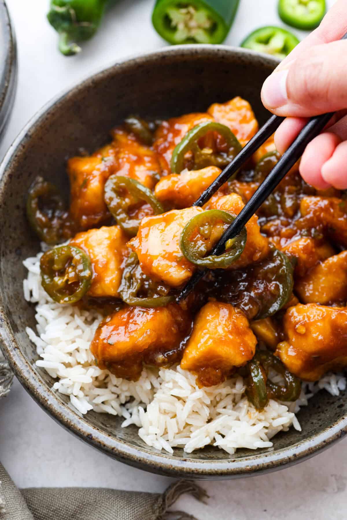 Delicious Jalapeño Chicken will become an instant favorite with the very first bite. Tender chicken pieces are cooked with jalapeños and then coated in a sticky, sweet, and spicy sauce. Serve over rice for an easy meal. You'll be craving it on repeat! Close up shot of someone using chopsticks to get a bite of the plated jalapeño chicken.