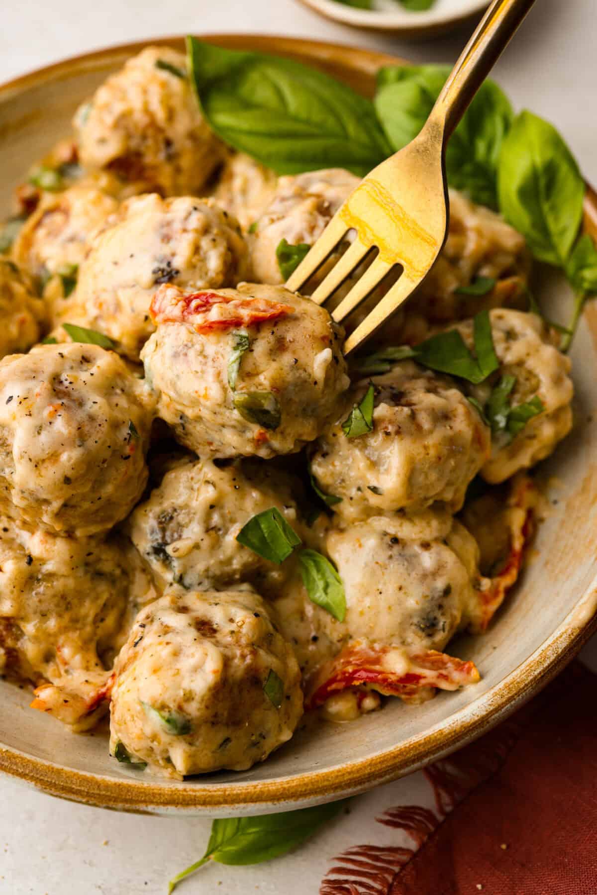 With creamy Tuscan flavors, these Marry Me Meatballs are an instant crowd favorite! It doesn't get much better than Italian seasoned chicken meatballs nestled in a creamy, cheesy sauce with sun-dried tomatoes and fresh herbs. Close up shot of plated marry me meatballs with a fork in one of them.