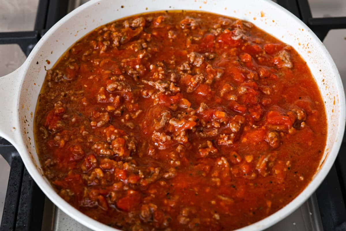 Million Dollar Ravioli Casseroleย is a flavorful casserole version of the classic! It's easy to make with mouthwatering layers of cheesy ravioli, meat sauce, and melted mozzarella cheese on top. This is a comforting, family-friendly dinner that you'll be craving on repeat! Overhead shot of browned meat and seasonings with marinara sauce poured over the top in a skillet.