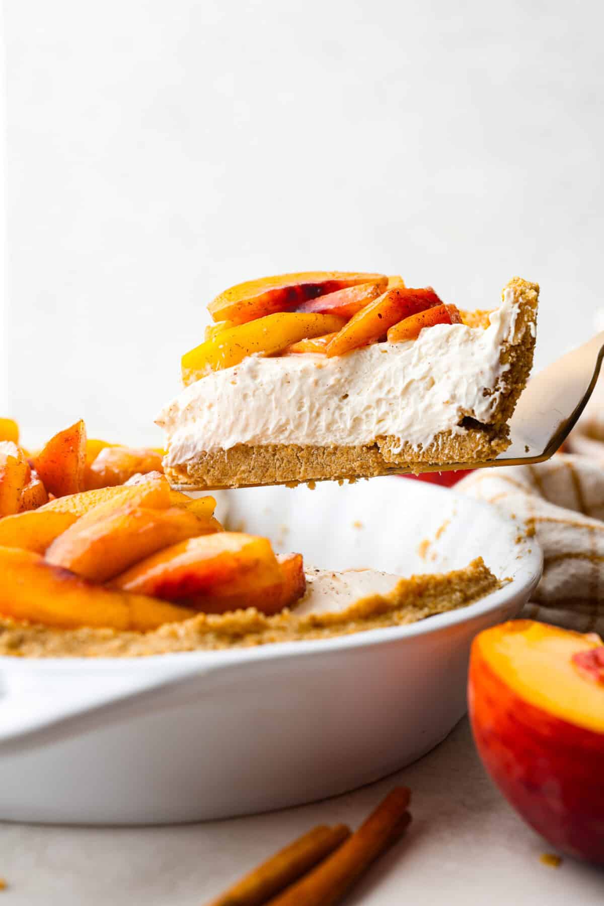 Enjoy juicy, ripe peaches in this Fresh Peach Pie. It has a creamy cheesecake filling topped with sweet peaches, all nestled in a buttery graham cracker crust. Itโs simply delightful, and no baking is required! Side shot of a slice of fresh peach pie being lifted out of the pie pan.
