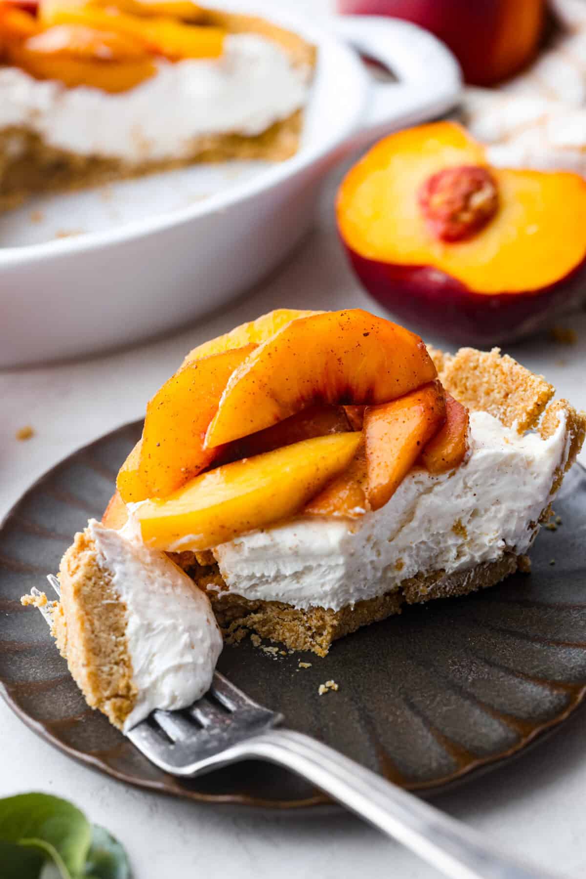Enjoy juicy, ripe peaches in this Fresh Peach Pie. It has a creamy cheesecake filling topped with sweet peaches, all nestled in a buttery graham cracker crust. Itโs simply delightful, and no baking is required! Angle shot of a plated slice of the no-bake fresh peach pie.