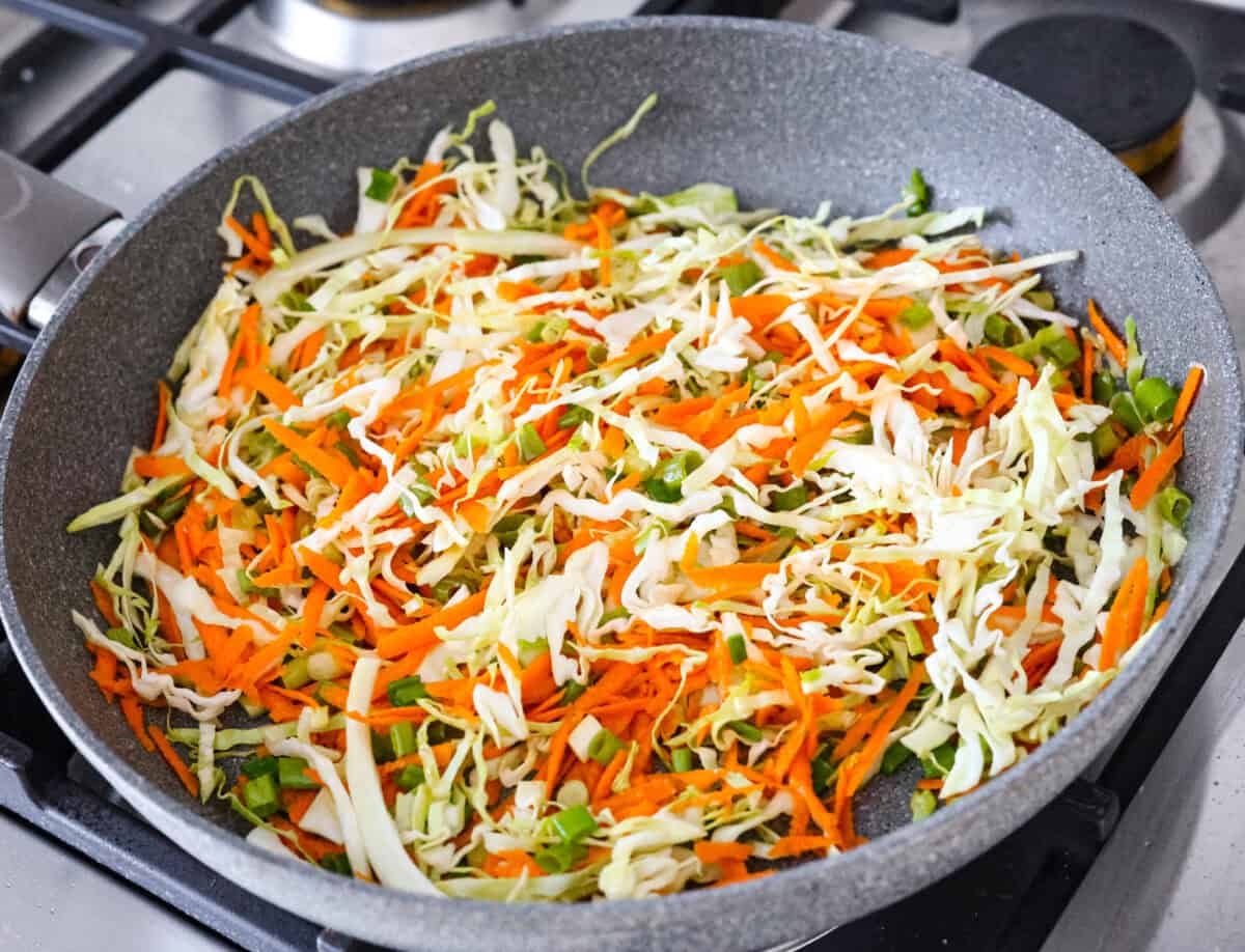Crispy outside with a warm, flavorful filling, these Shrimp Egg Rolls are beyond delicious! They're packed with a mix of vermicelli noodles, sautéed veggies, shrimp and plenty of flavorings, then fried till crunchy and golden brown. Serve them as an appetizer, a light main or party side dish! Overhead shot of vegetables cooking in a skillet.