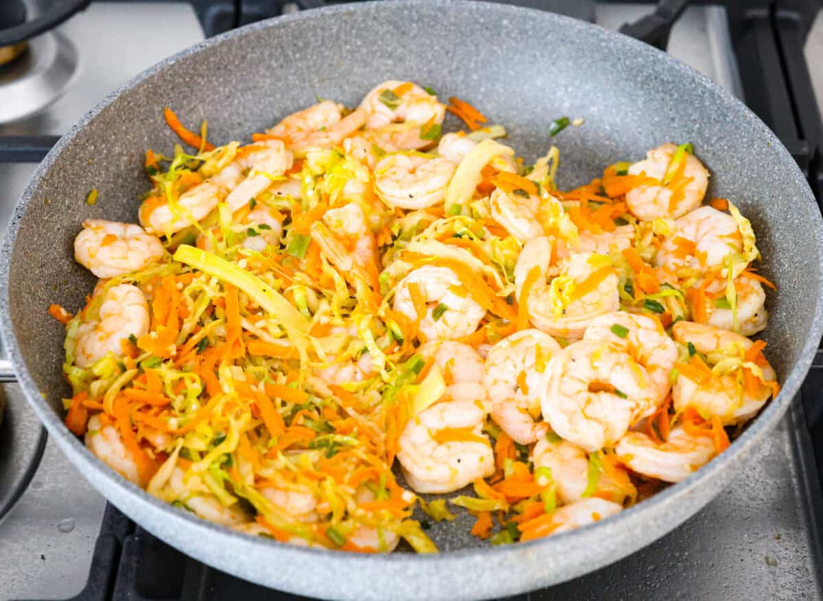 Crispy outside with a warm, flavorful filling, these Shrimp Egg Rolls are beyond delicious! They're packed with a mix of vermicelli noodles, sautéed veggies, shrimp and plenty of flavorings, then fried till crunchy and golden brown. Serve them as an appetizer, a light main or party side dish! Overhead shot of shrimp and seasonings and sauces mixed in with the vegetables in a skillet.
