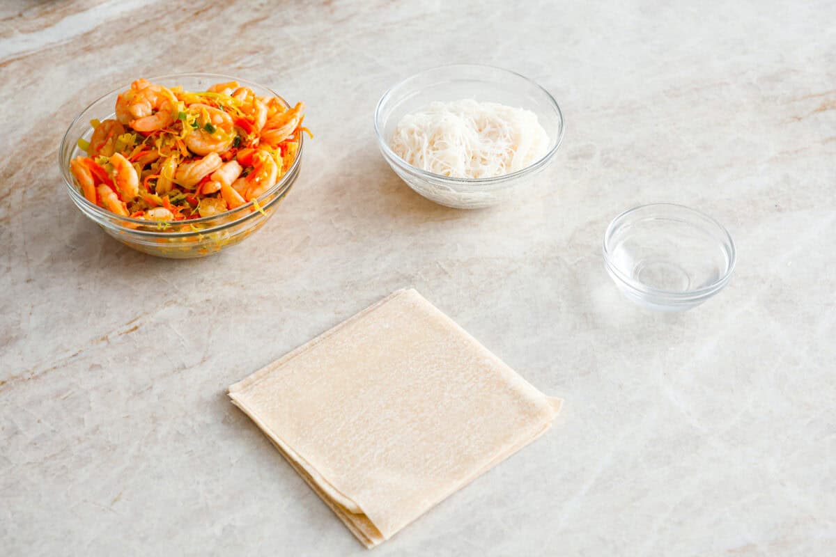 Crispy outside with a warm, flavorful filling, these Shrimp Egg Rolls are beyond delicious! They're packed with a mix of vermicelli noodles, sautéed veggies, shrimp and plenty of flavorings, then fried till crunchy and golden brown. Serve them as an appetizer, a light main or party side dish! Angle shot of prepped work station.