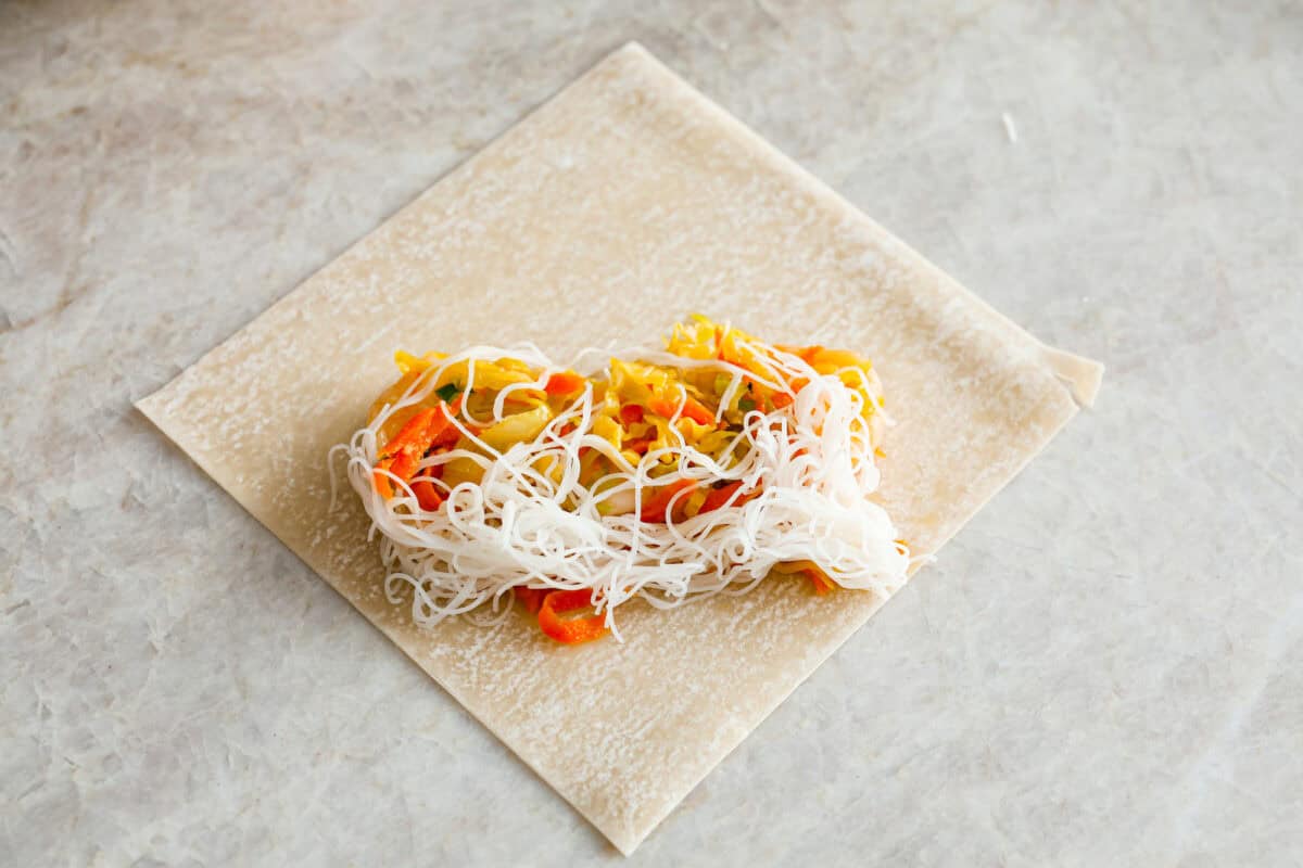 Crispy outside with a warm, flavorful filling, these Shrimp Egg Rolls are beyond delicious! They're packed with a mix of vermicelli noodles, sautéed veggies, shrimp and plenty of flavorings, then fried till crunchy and golden brown. Serve them as an appetizer, a light main or party side dish! Overhead shot of noodles and veggie filling on an egg roll wrapper.