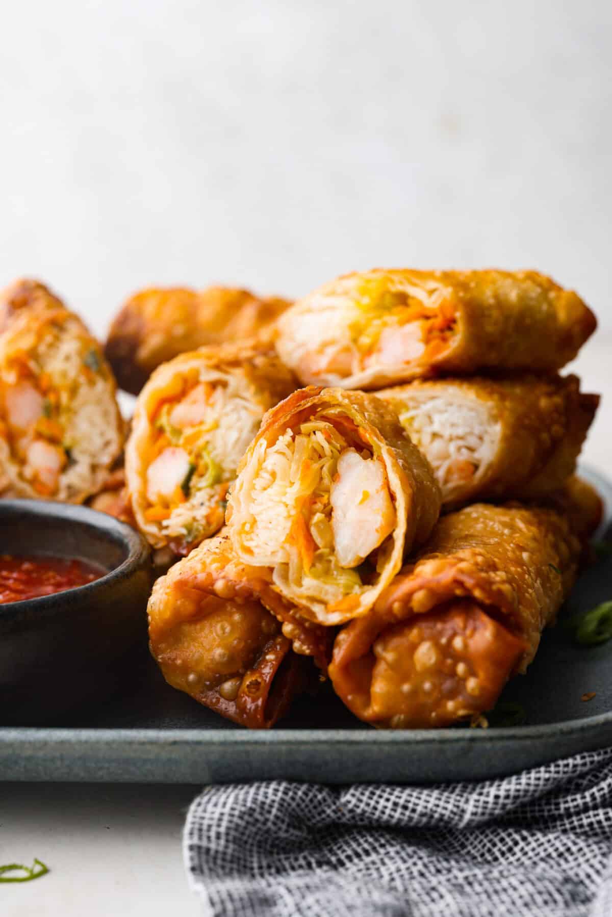 Crispy outside with a warm, flavorful filling, these Shrimp Egg Rolls are beyond delicious! They're packed with a mix of vermicelli noodles, sautéed veggies, shrimp and plenty of flavorings, then fried till crunchy and golden brown. Serve them as an appetizer, a light main or party side dish! Side shot of egg rolls stacked on a plate with some of the rolls cut in half.