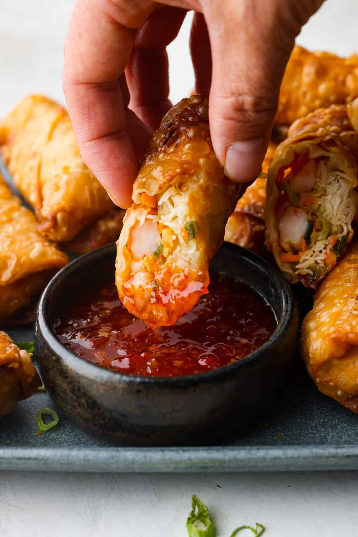 Crispy outside with a warm, flavorful filling, these Shrimp Egg Rolls are beyond delicious! They're packed with a mix of vermicelli noodles, sautéed veggies, shrimp and plenty of flavorings, then fried till crunchy and golden brown. Serve them as an appetizer, a light main or party side dish! Close up shot of someone dipping a shrimp egg roll in sauce.