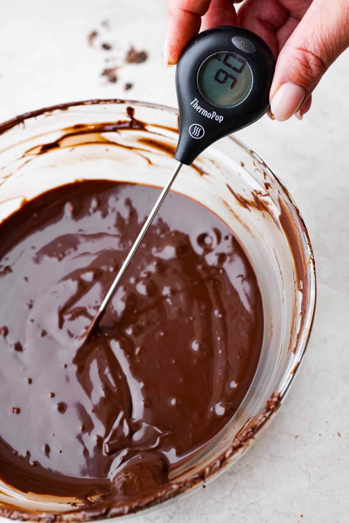 Learn how to temper chocolate for all your chocolate dipping and candy-making needs! Tempering chocolate can be intimidating but my how-to guide will help you every step of the way. Close view of a thermometer testing the temperature of a bowl of melted chocolate.