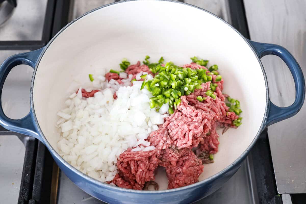 This creamy taco soup recipe is full of fresh flavors, tender vegetables, and hearty beans. The seasoned beef mixed with the creamy soup is out of this world good! Top it with your favorite toppings, and your family will love this warm, savory soup! Angle shot of beef, onions and jalapeños in a pot.