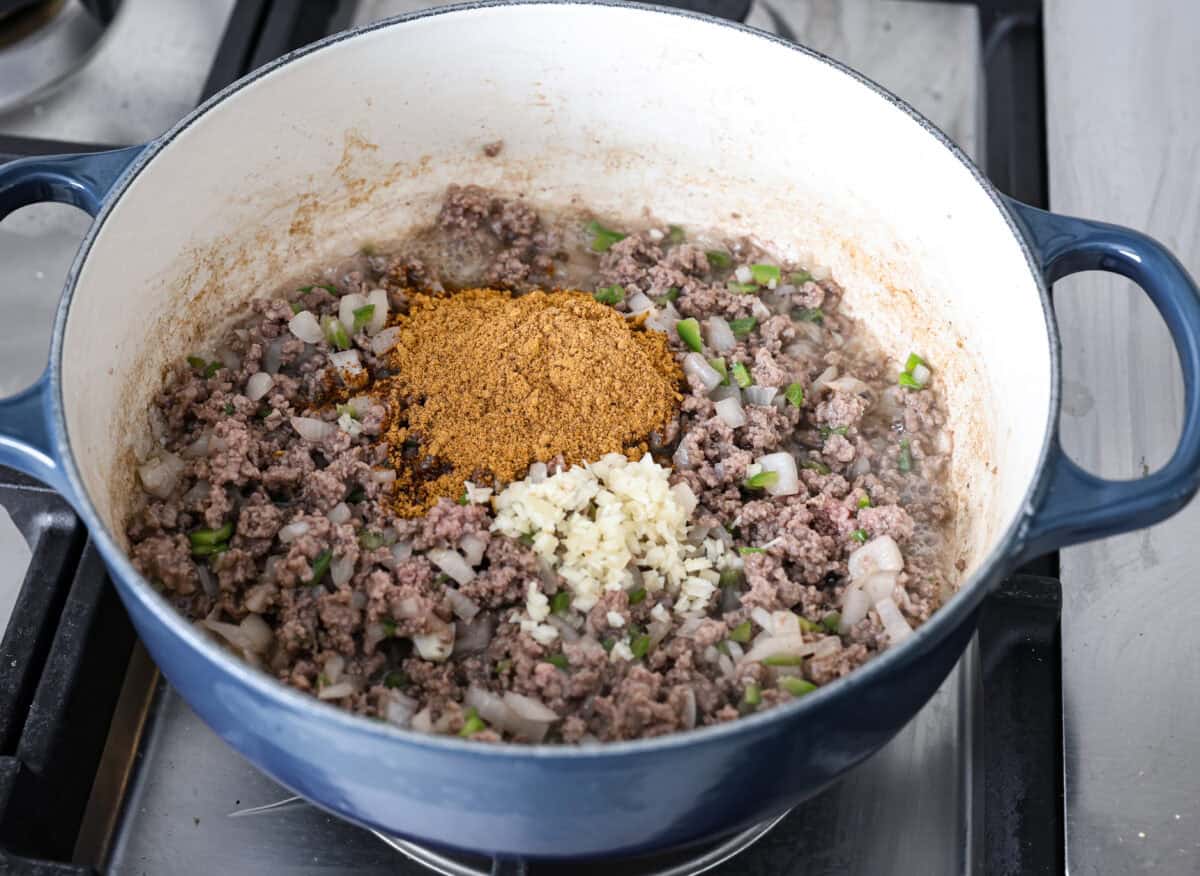 This creamy taco soup recipe is full of fresh flavors, tender vegetables, and hearty beans. The seasoned beef mixed with the creamy soup is out of this world good! Top it with your favorite toppings, and your family will love this warm, savory soup! Angle shot of cooked beef mixture with minced garlic and taco seasoning added to it.