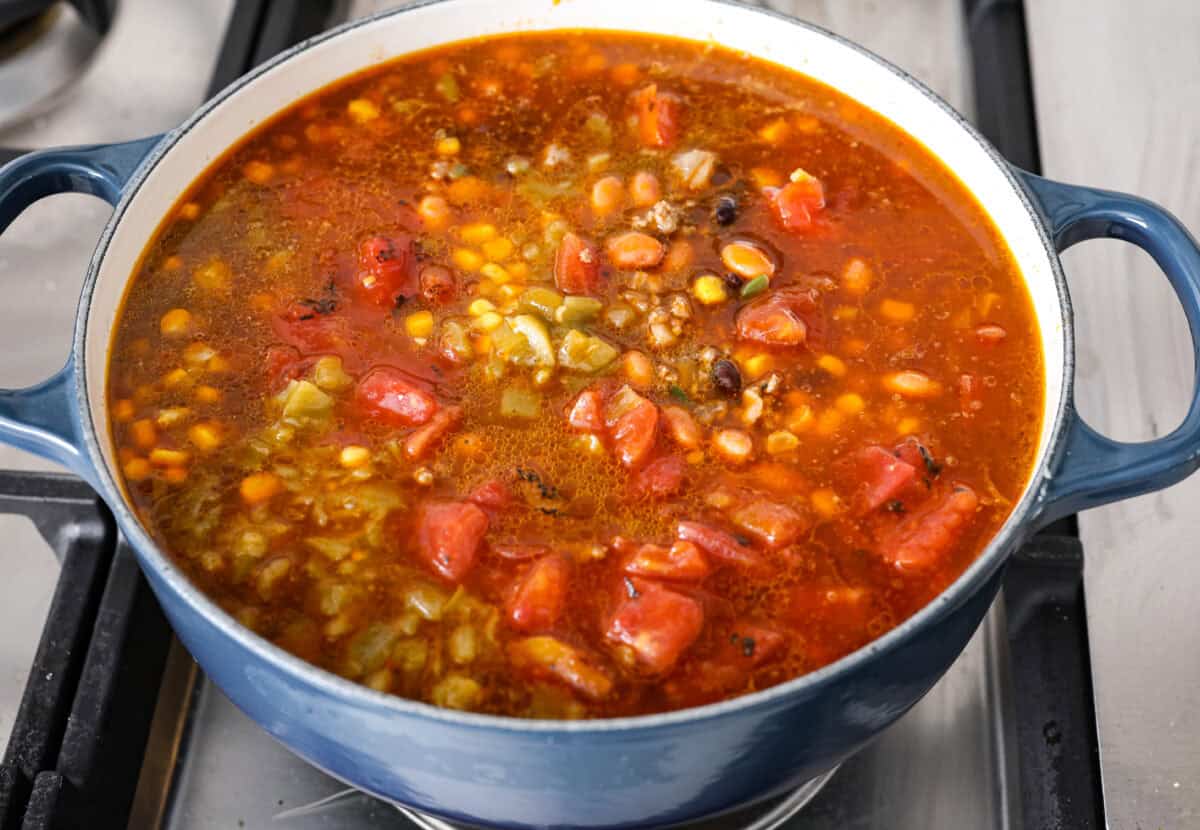 This creamy taco soup recipe is full of fresh flavors, tender vegetables, and hearty beans. The seasoned beef mixed with the creamy soup is out of this world good! Top it with your favorite toppings, and your family will love this warm, savory soup! Angle shot of beef mixture with all of the canned vegetables and beef broth added to it.