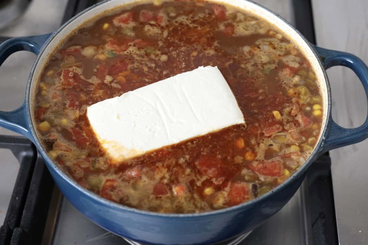 This creamy taco soup recipe is full of fresh flavors, tender vegetables, and hearty beans. The seasoned beef mixed with the creamy soup is out of this world good! Top it with your favorite toppings, and your family will love this warm, savory soup! Angle shot of the soup mixture with a block of cream cheese added in the middle.
