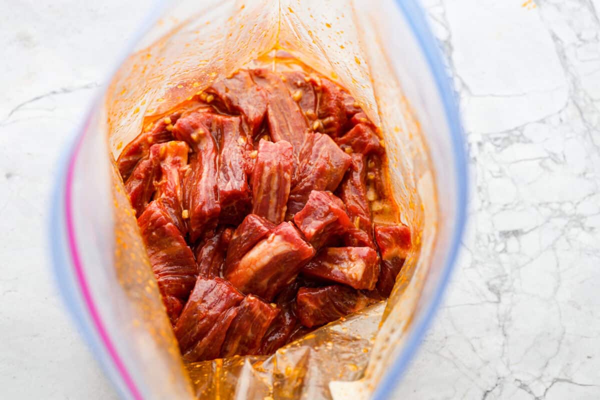 Kung Pao Beef is just like your favorite takeout but way tastier! This dish is loaded with flavor and so easy to make. Tender, marinated beef is stir-fried with veggies in a tangy, spicy Asian sauceย for an unforgettable meal! Overhead shot of beef in marinade in a ziplock bag.