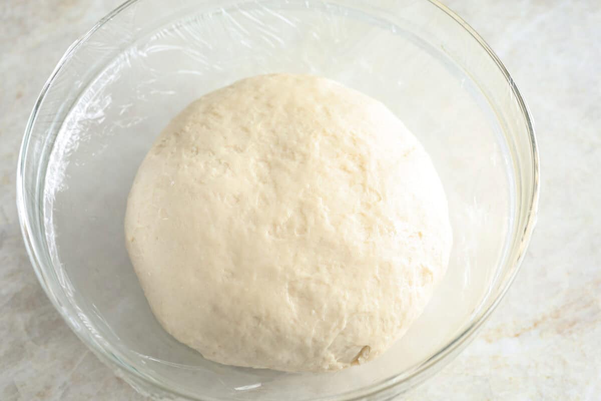 Bao Buns, or Baozi, are soft, pillowy buns made from a slightly sweet dough. They originate from China and are served with different types of fillings. You can enjoy them as a snack, as a side, or with dim sum. Overhead shot of a bao bun dough ball in the bottom of an oiled glass bowl.