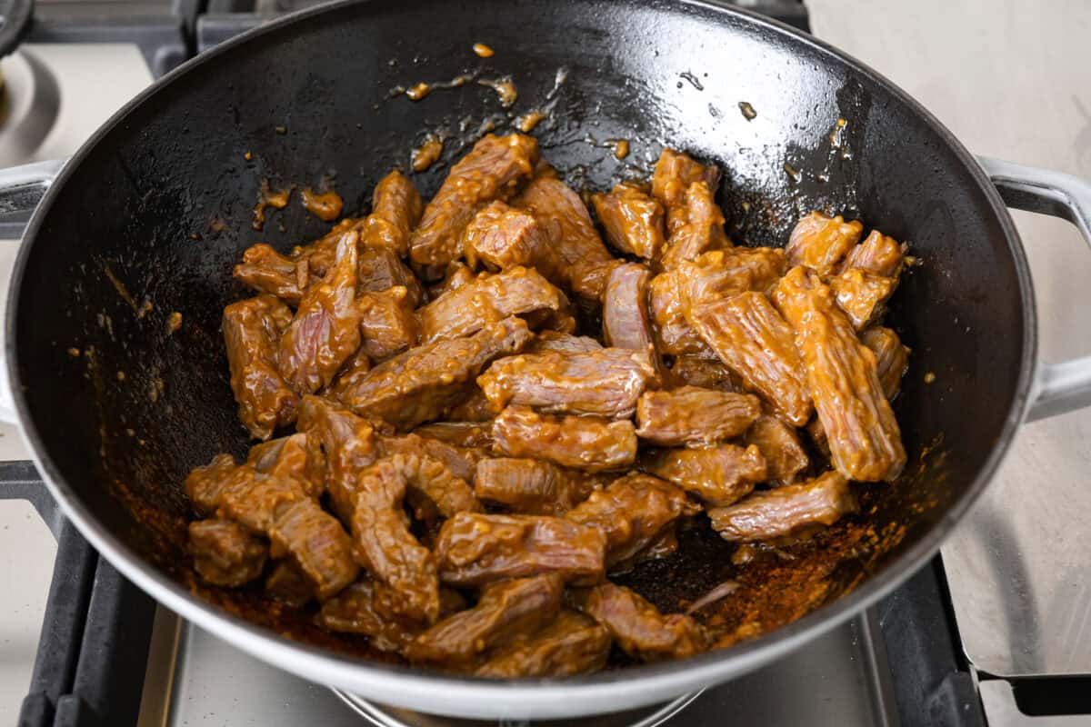 Kung Pao Beef is just like your favorite takeout but way tastier! This dish is loaded with flavor and so easy to make. Tender, marinated beef is stir-fried with veggies in a tangy, spicy Asian sauceย for an unforgettable meal! Angle shot of marinated beef cooking in a wok.