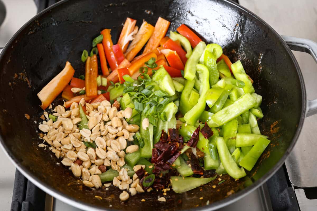 Kung Pao Beef is just like your favorite takeout but way tastier! This dish is loaded with flavor and so easy to make. Tender, marinated beef is stir-fried with veggies in a tangy, spicy Asian sauceย for an unforgettable meal! Angle shot of veggies peanuts and dried chilies in the wok.