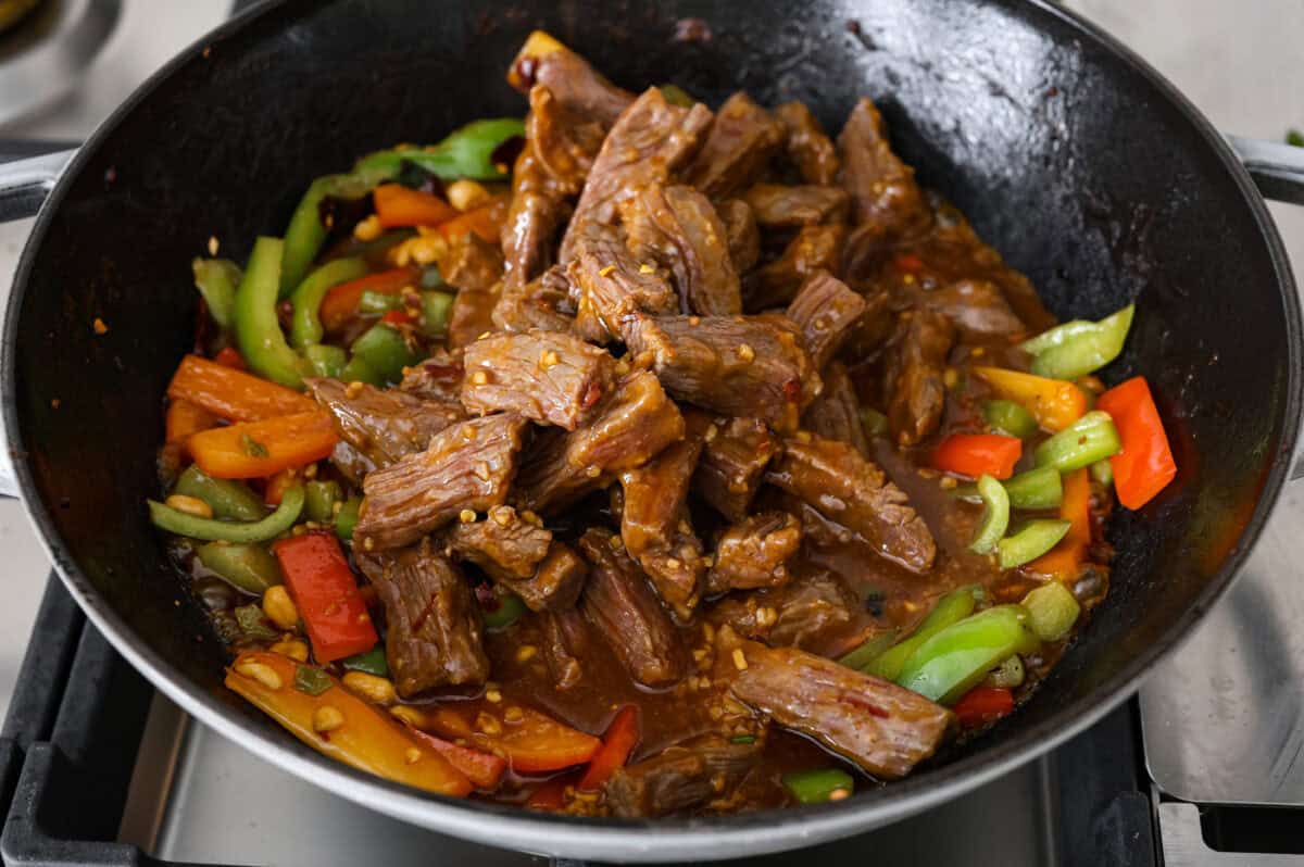 Kung Pao Beef is just like your favorite takeout but way tastier! This dish is loaded with flavor and so easy to make. Tender, marinated beef is stir-fried with veggies in a tangy, spicy Asian sauceย for an unforgettable meal! Close up shot of cooked kung pao beef being added back to the wok with the veggies.