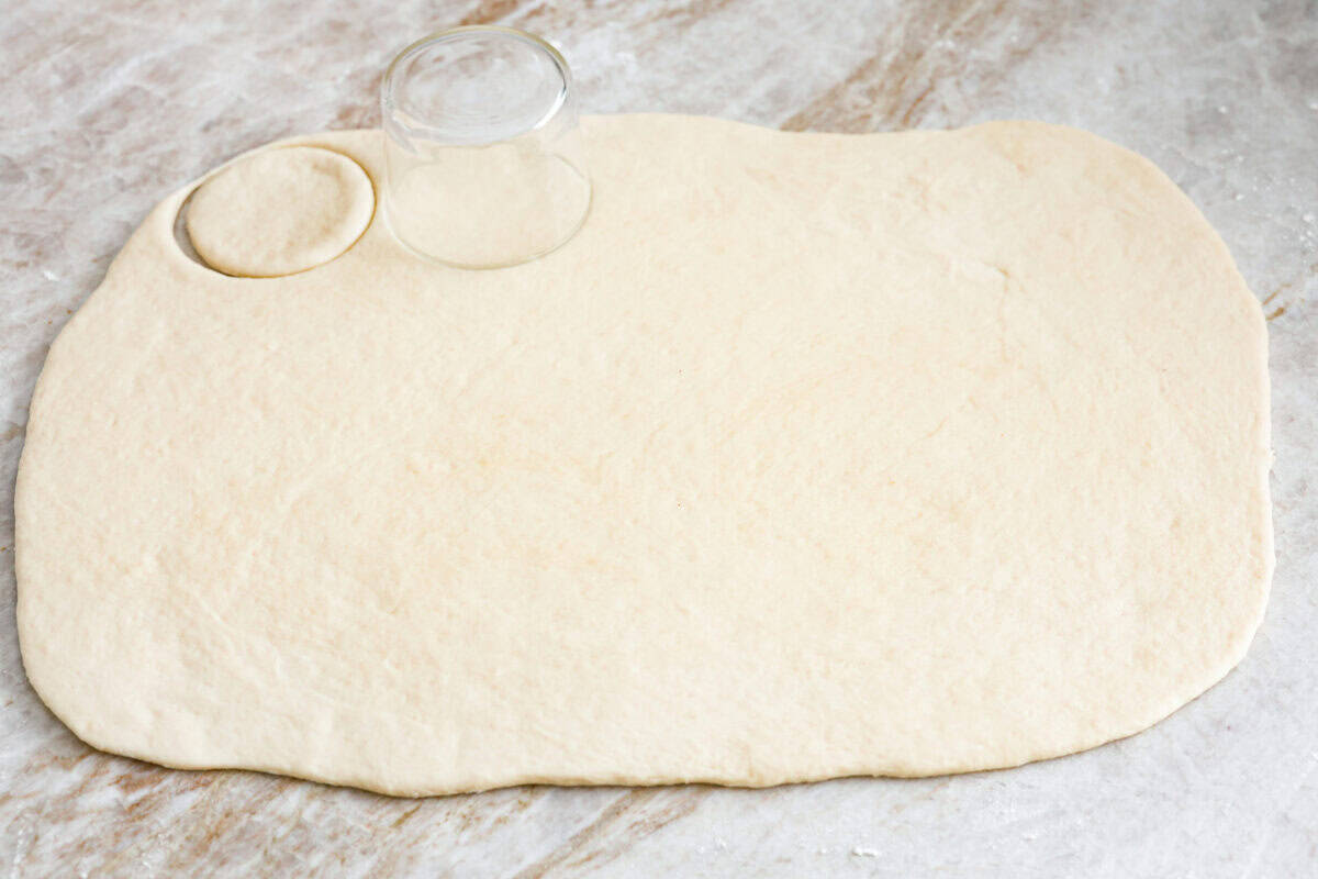Bao Buns, or Baozi, are soft, pillowy buns made from a slightly sweet dough. They originate from China and are served with different types of fillings. You can enjoy them as a snack, as a side, or with dim sum. Angle shot of rolled out bao bun dough being cut into circles.