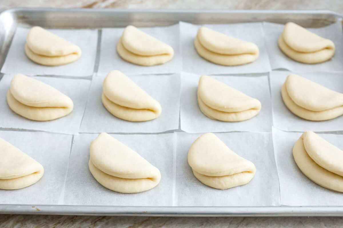 Bao Buns, or Baozi, are soft, pillowy buns made from a slightly sweet dough. They originate from China and are served with different types of fillings. You can enjoy them as a snack, as a side, or with dim sum. Angle shot of boa bun circles folded in half on parchment paper on a baking sheet.