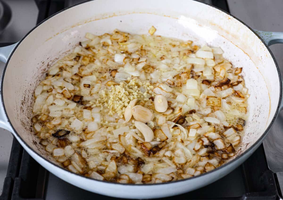 Chicken korma is a traditional Indian chicken dish. It's made with tender chicken smothered in a creamy, wonderfully seasoned sauce. It's so good your family will think you got takeout! Angle shot of onions garlic and ginger being sautéed in the ghee and oil.