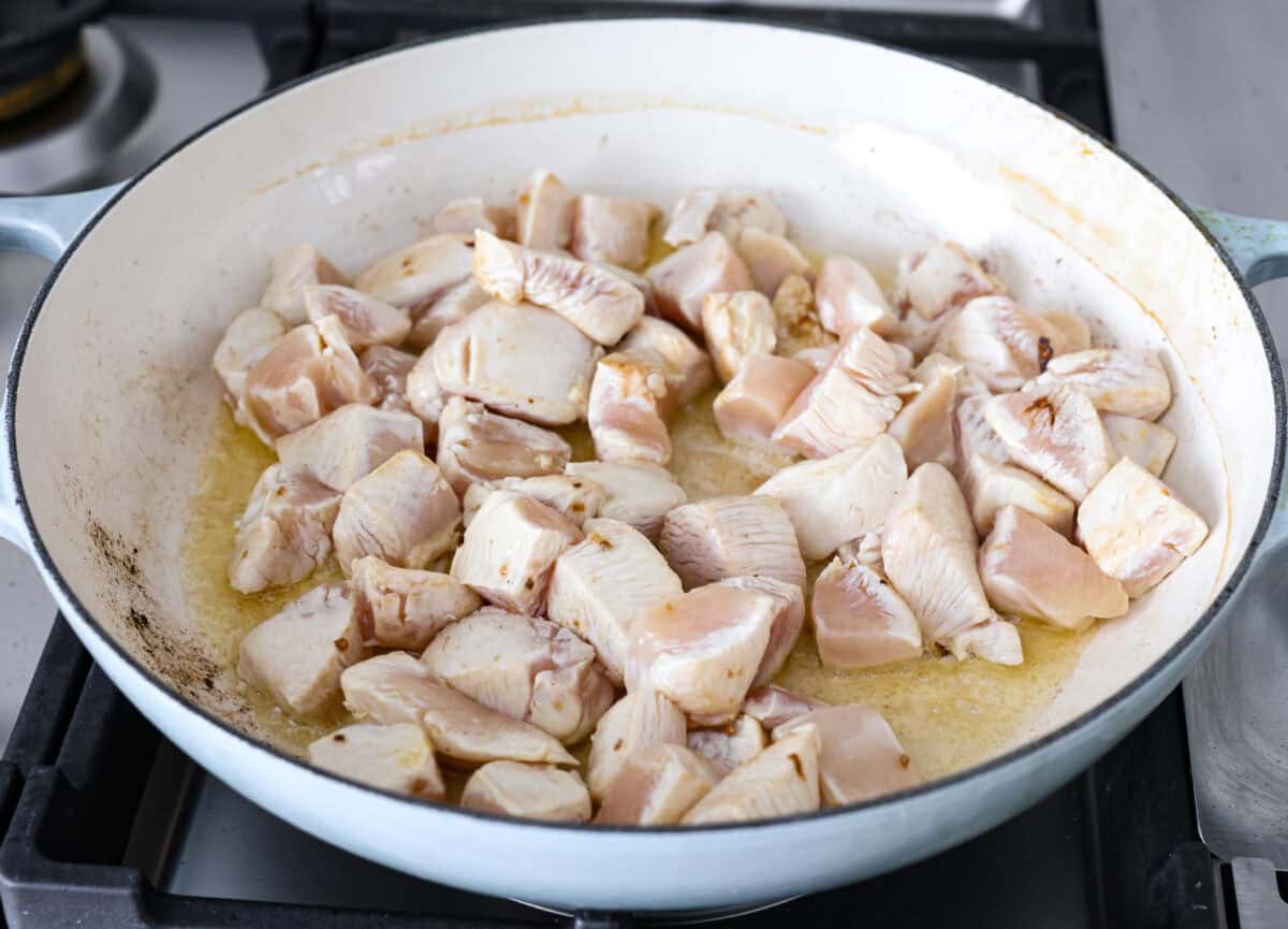 Chicken korma is a traditional Indian chicken dish. It's made with tender chicken smothered in a creamy, wonderfully seasoned sauce. It's so good your family will think you got takeout! Angle shot of chicken being searing in oil and ghee in a skillet.