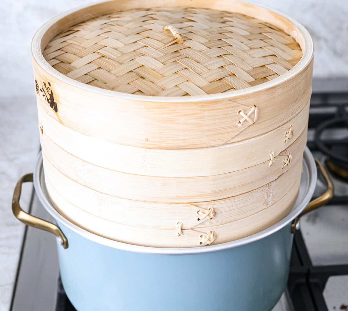 Bao Buns, or Baozi, are soft, pillowy buns made from a slightly sweet dough. They originate from China and are served with different types of fillings. You can enjoy them as a snack, as a side, or with dim sum. Side shot of pot with boiling water, fitted with a steam ring and a bamboo steam on top.