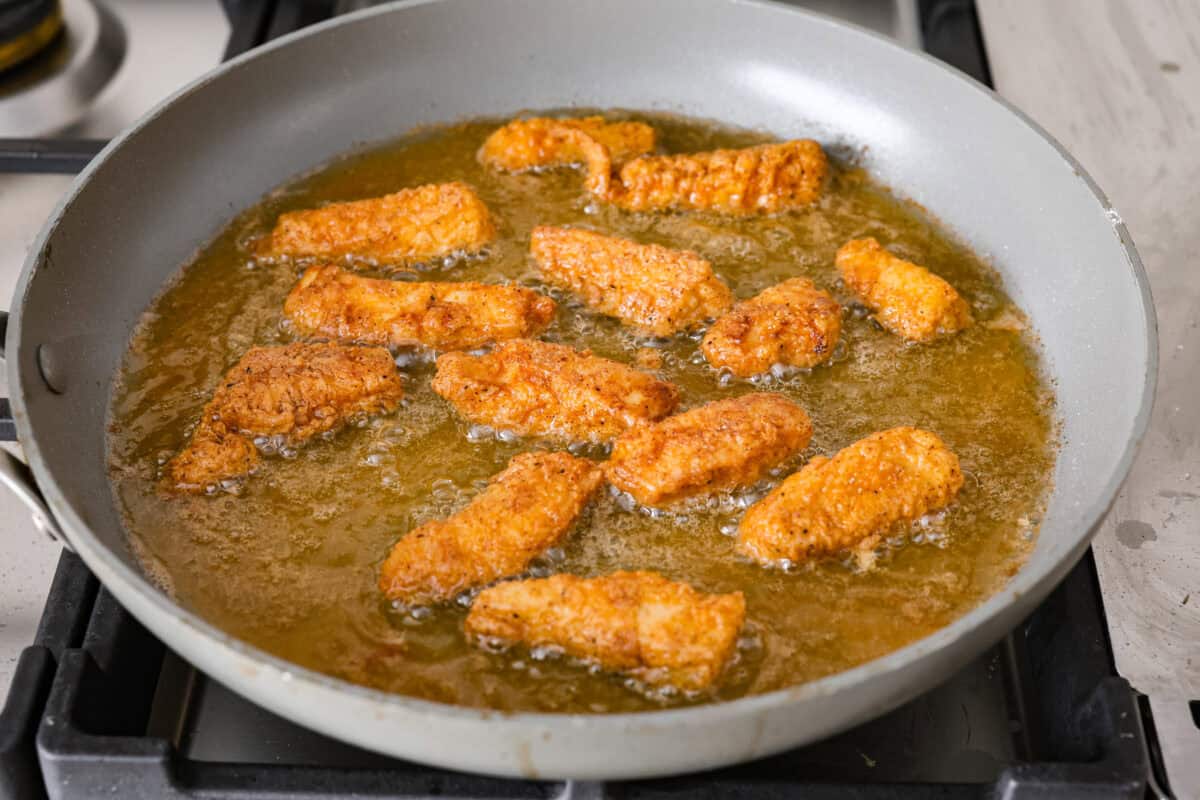 Dragon Chicken is a spicy and flavorful dish featuring tender breaded chicken stir-fried with vegetables and coated in a rich, tangy, and slightly sweet sauce. It's a crowd favorite for those who enjoy a fiery twist on the classic stir-fry! Angle shot of breaded chicken being fried in a skillet.