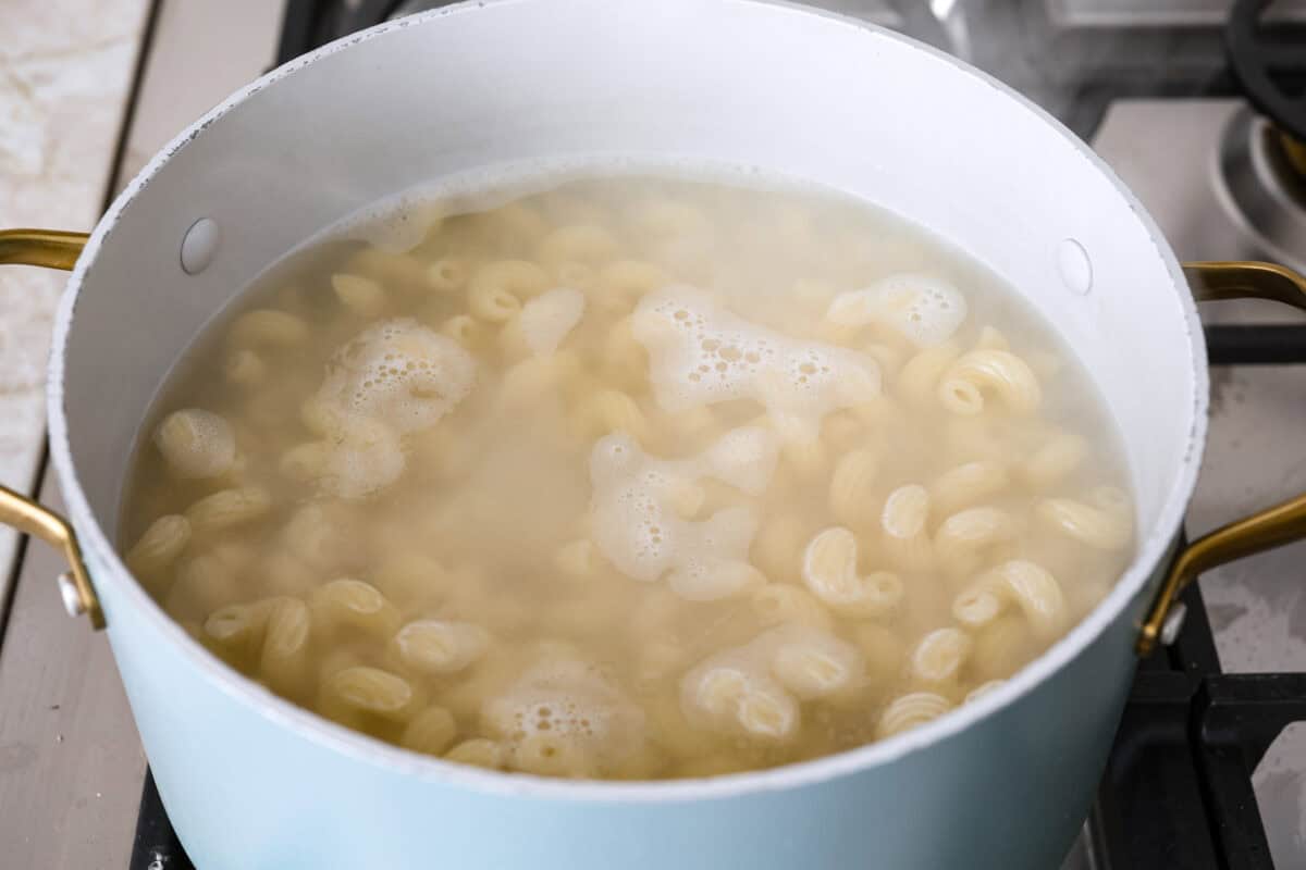 This Boursin pasta recipe has gone viral on social media. It's simple to make and packed with flavor! It's creamy with a distinct zingy bite from the Boursin cheese and sundried tomatoes. This dish screams flavor! It's anything but boring. Angle shot of pasta cooked in boiling water.
