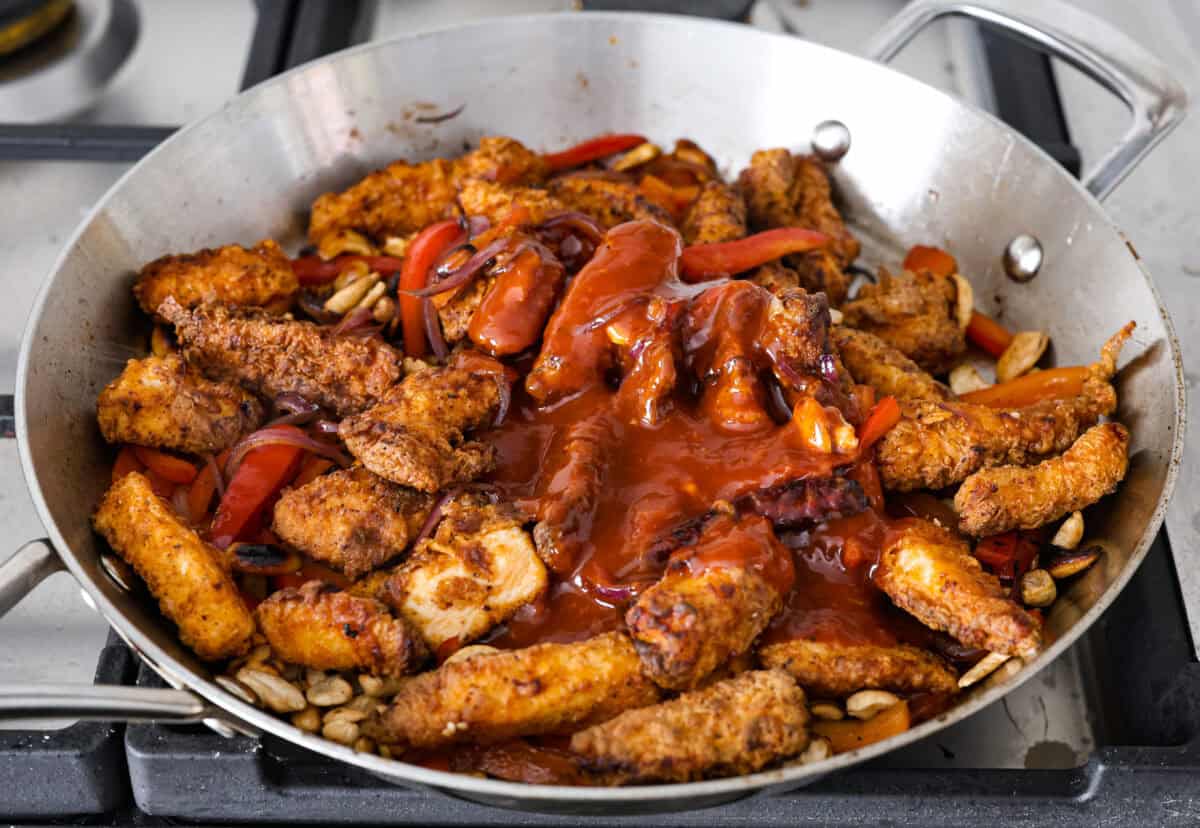Dragon Chicken is a spicy and flavorful dish featuring tender breaded chicken stir-fried with vegetables and coated in a rich, tangy, and slightly sweet sauce. It's a crowd favorite for those who enjoy a fiery twist on the classic stir-fry! Close up shot of fried chicken, stir fried veggies covered in sauce in a wok.