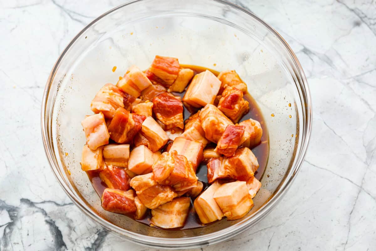 This simple air fryer pork belly recipe is great for making and enjoying this indulgent snack. It's meaty, crispy, smothered in a sticky, salty marinade that sets the flavors off perfectly! Overhead shot of meat in marinade in bowl.