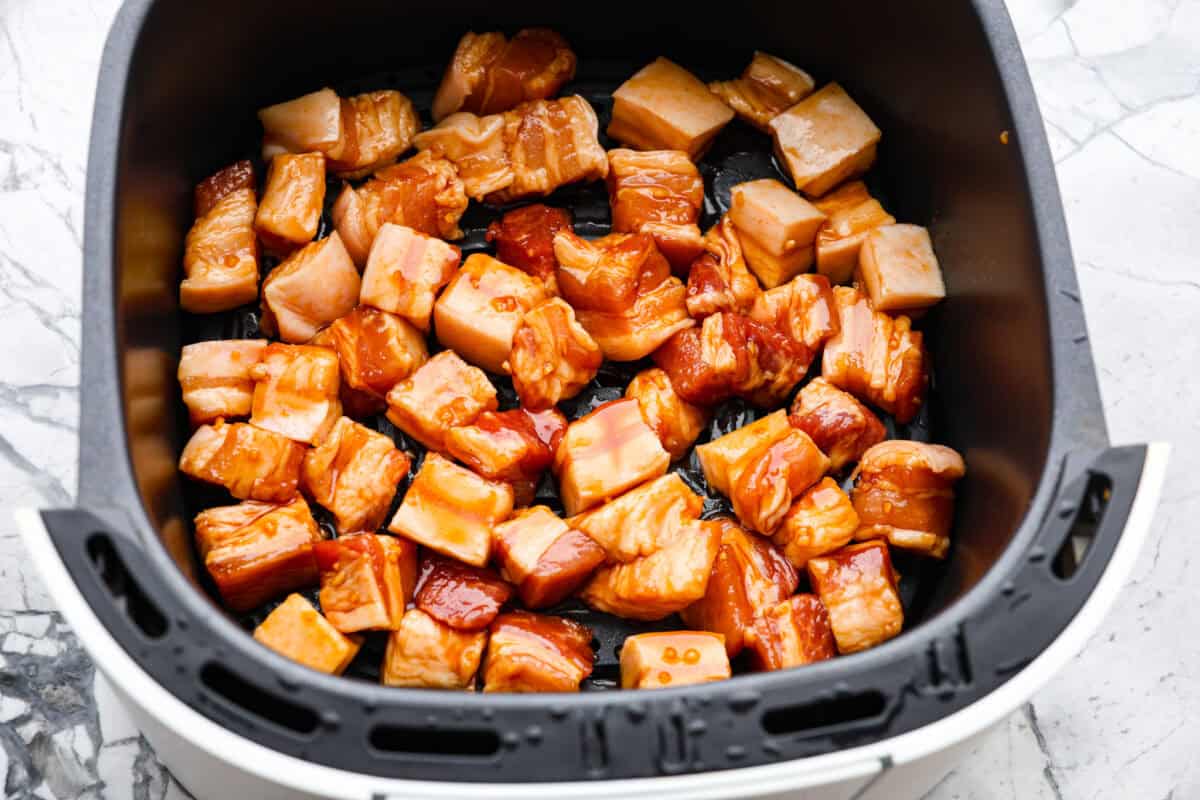 This simple air fryer pork belly recipe is great for making and enjoying this indulgent snack. It's meaty, crispy, smothered in a sticky, salty marinade that sets the flavors off perfectly! Overhead shot of marinated pole in the air fryer basket.