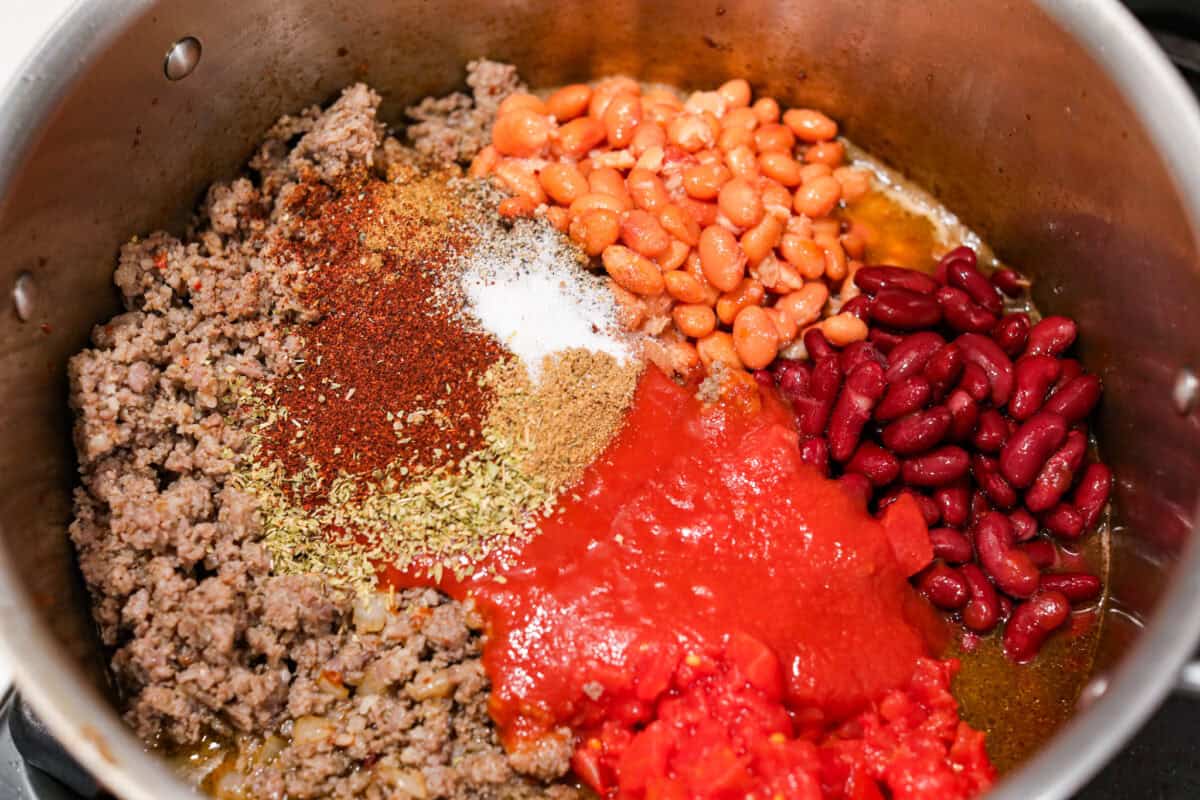 Breakfast Chili is comforting, tasty and will fill you up for hours! A combination of sausage, bacon, tomato sauce, beans, and plenty of tasty seasonings come together for a unique morning meal you will love! Top it off with fried eggs and fresh cilantro for major flavor! Overhead shot of the beans, seasonings, and tomatoes added to the bacon and sausage.