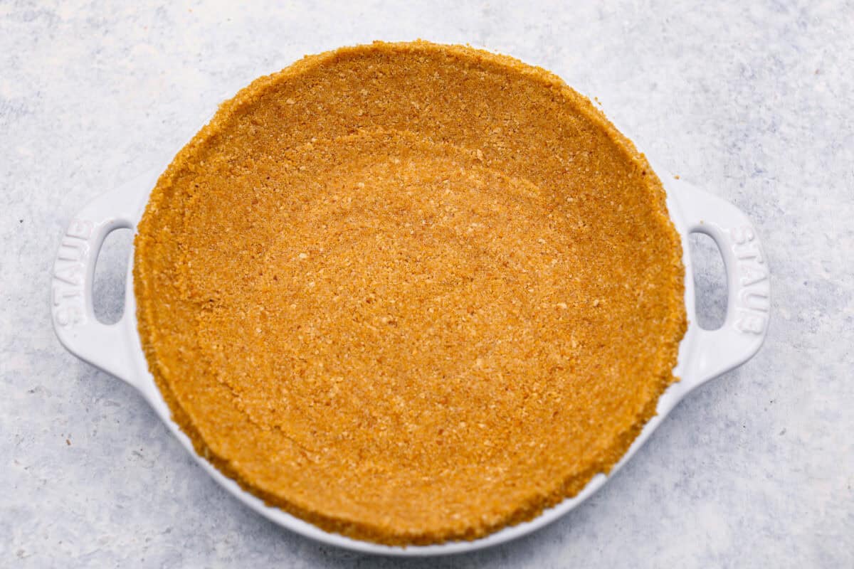 Learn how to make the perfect homemade Graham Cracker Crust! It comes together in just 10 minutes with 3 simple ingredients for the right amount of buttery sweetness and crunch!ย Youโll never buy one from the store again! Overhead shot of crust pressed into a pie dish.