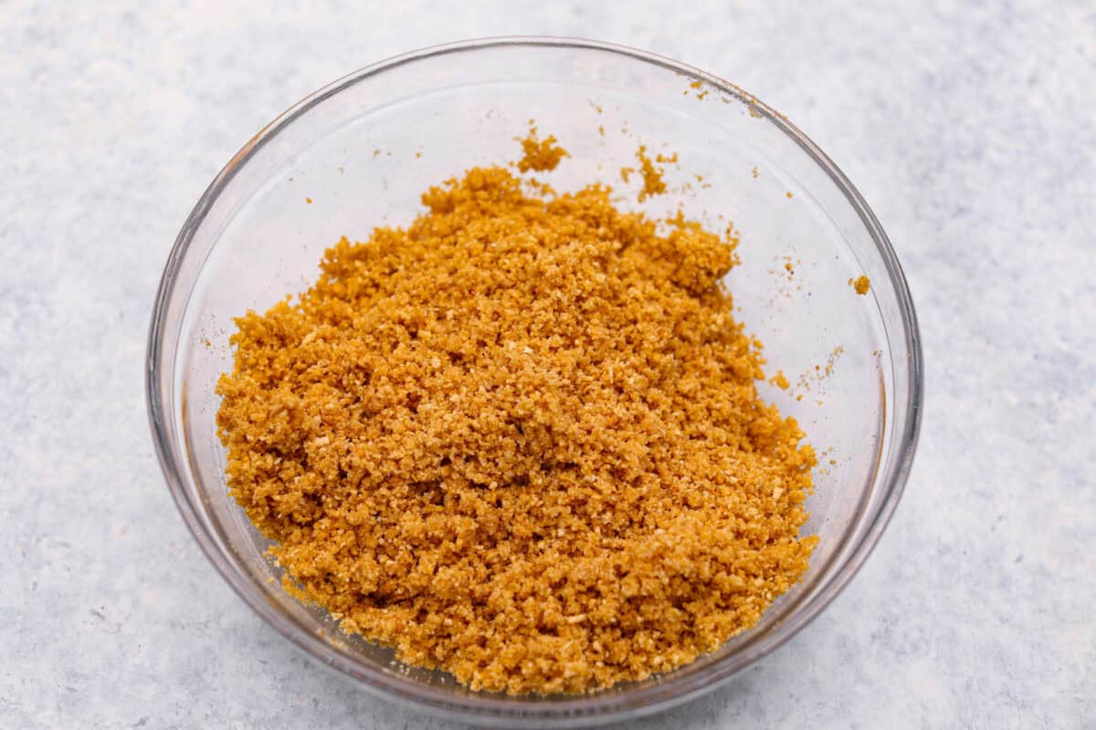 Learn how to make the perfect homemade Graham Cracker Crust! It comes together in just 10 minutes with 3 simple ingredients for the right amount of buttery sweetness and crunch!ย Youโll never buy one from the store again! Overhead shot of melted butter, sugar and graham cracker crumbs mixed in a bowl.