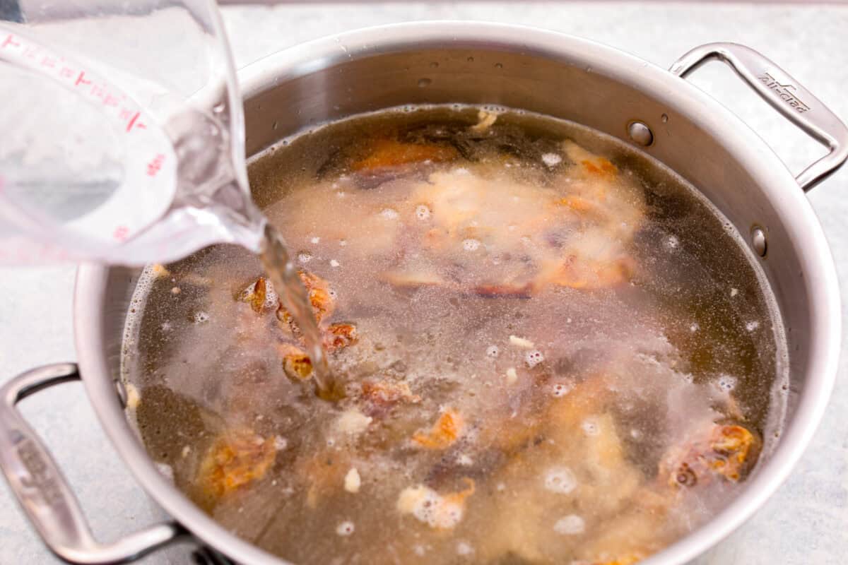 Learn how to make homemade bone broth with all of my top tips and tricks! This easy recipe is a simple combination of wholesome, nutritious ingredients. It's freezer-friendly and great for using in a variety of recipes, from soups, sauces and gravies to casseroles and rice. Angle shot of someone pouring water in to a pot of bones.