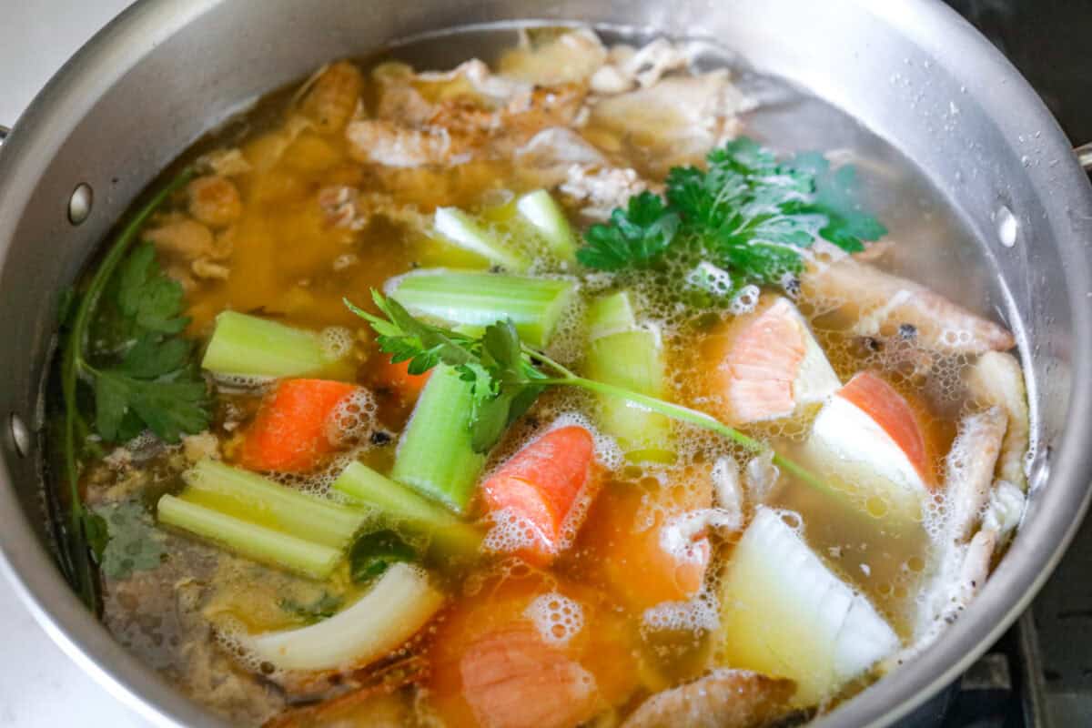 Learn how to make homemade bone broth with all of my top tips and tricks! This easy recipe is a simple combination of wholesome, nutritious ingredients. It's freezer-friendly and great for using in a variety of recipes, from soups, sauces and gravies to casseroles and rice. Angle shot of vegetables and herbs in the pot of water and bones simmering.