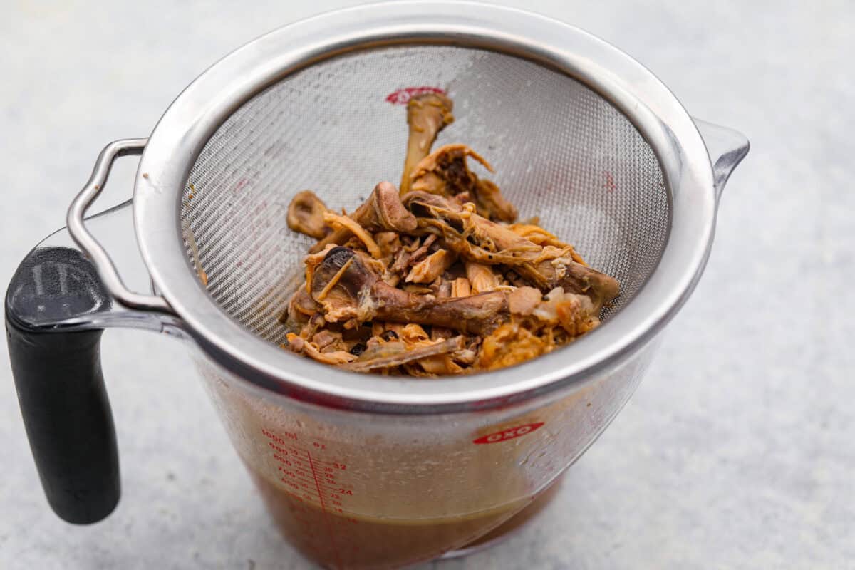 Learn how to make homemade bone broth with all of my top tips and tricks! This easy recipe is a simple combination of wholesome, nutritious ingredients. It's freezer-friendly and great for using in a variety of recipes, from soups, sauces and gravies to casseroles and rice. Angle shot of bones and skin being filtered out of the bone broth.