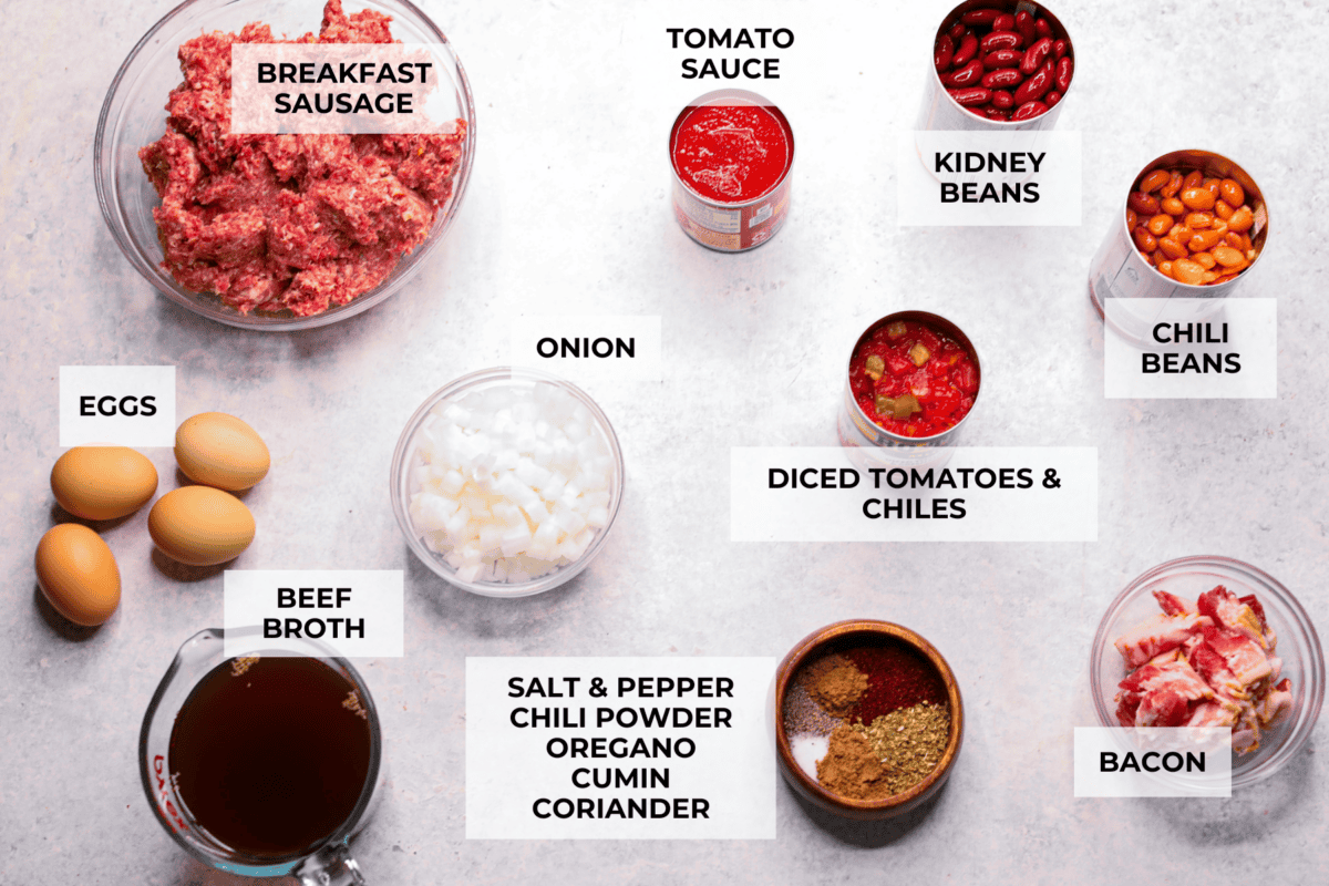 Breakfast Chili is comforting, tasty and will fill you up for hours! A combination of sausage, bacon, tomato sauce, beans, and plenty of tasty seasonings come together for a unique morning meal you will love! Top it off with fried eggs and fresh cilantro for major flavor! Overhead shot of labeled ingredients.