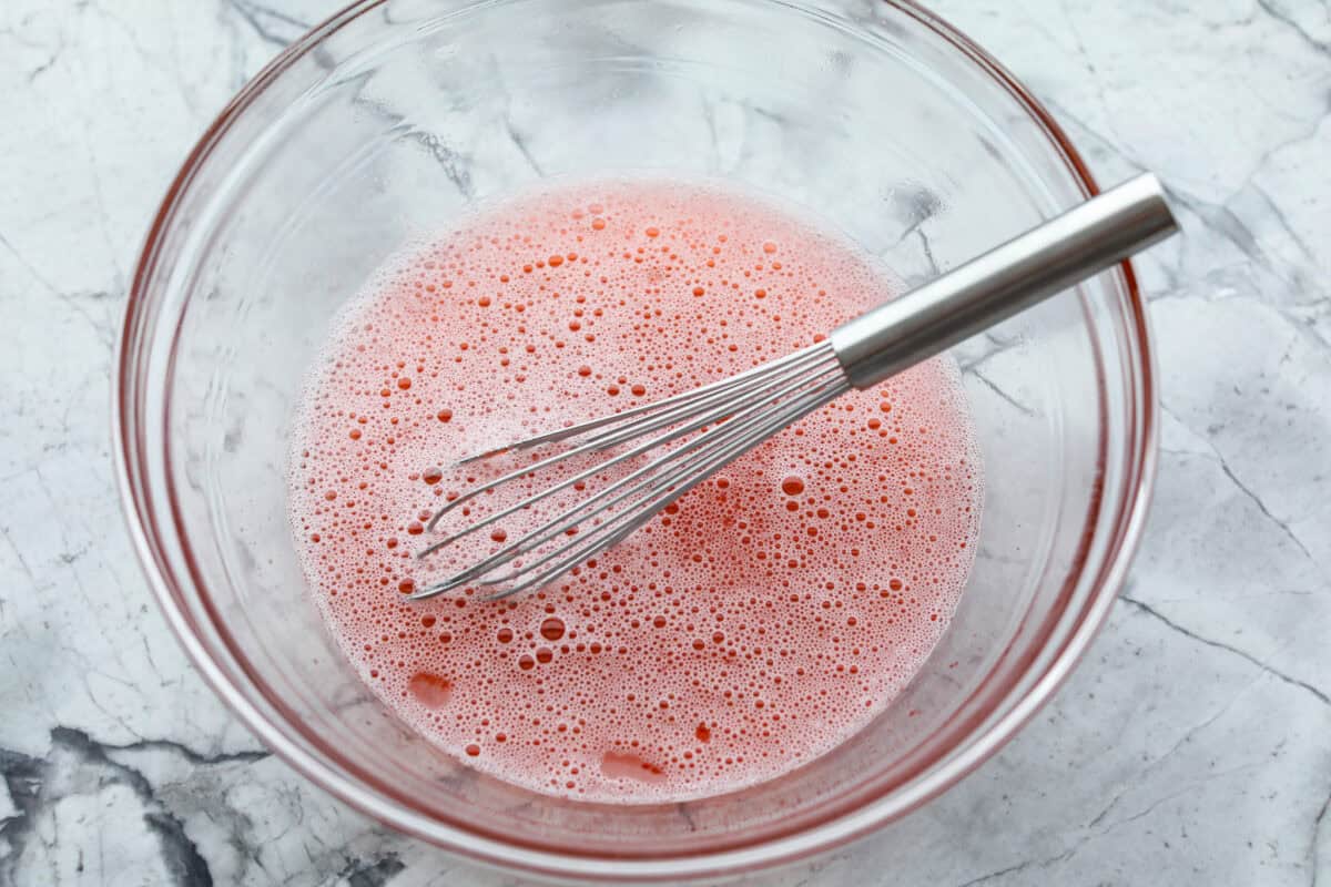 It's peach season which means you have to make this Peach Fluff Salad! It's a creamy, fruity dessert that hits all the right notes and is packed with fresh peaches! Jello and water in a glass bowl with a whisk.