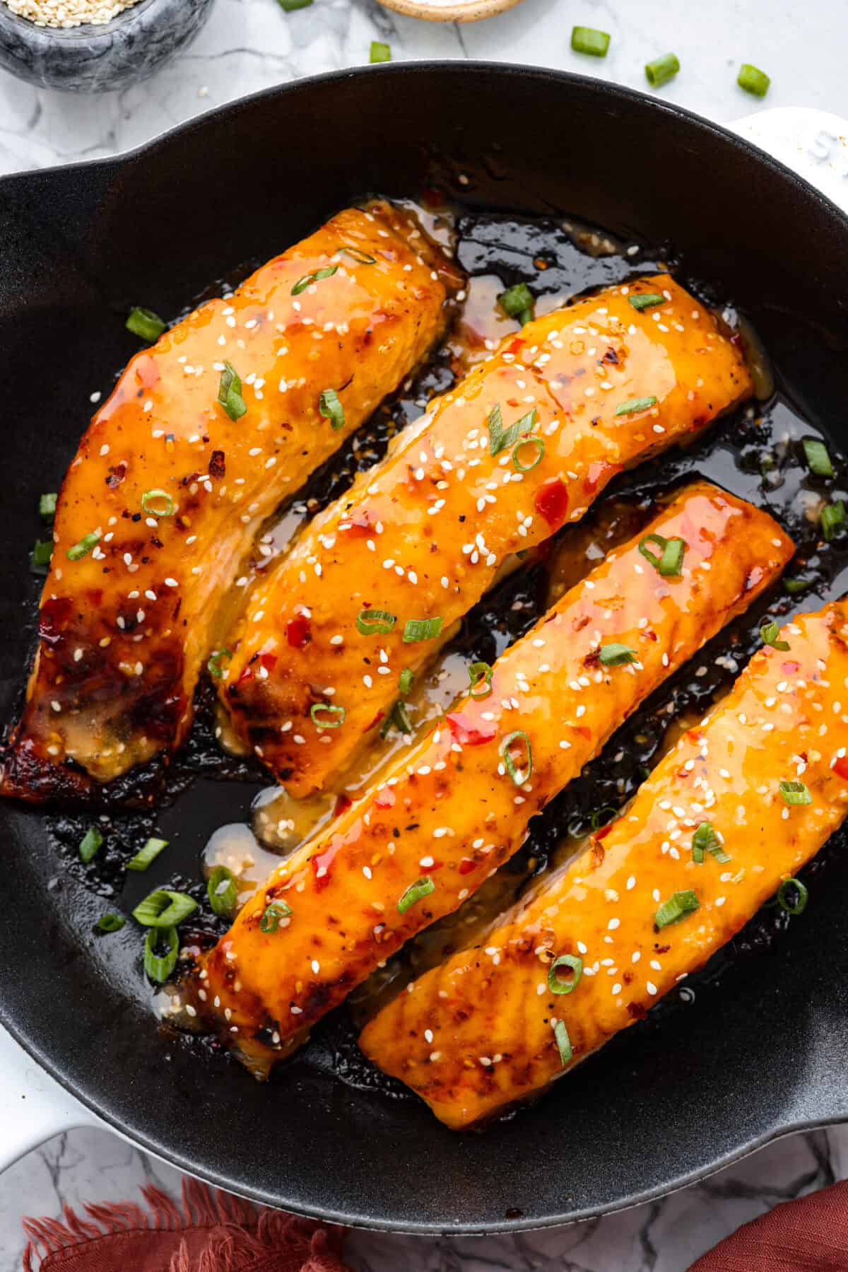 Bang Bang Salmon takes salmon filets, smothers them in bang bang sauce that is sweet with a kick, and then baked to perfection. You will love this simple yet oh-so-tasty dinner that can be ready to serve in less than 30 minutes! Overhead shot of bang bang salmon in a skillet.