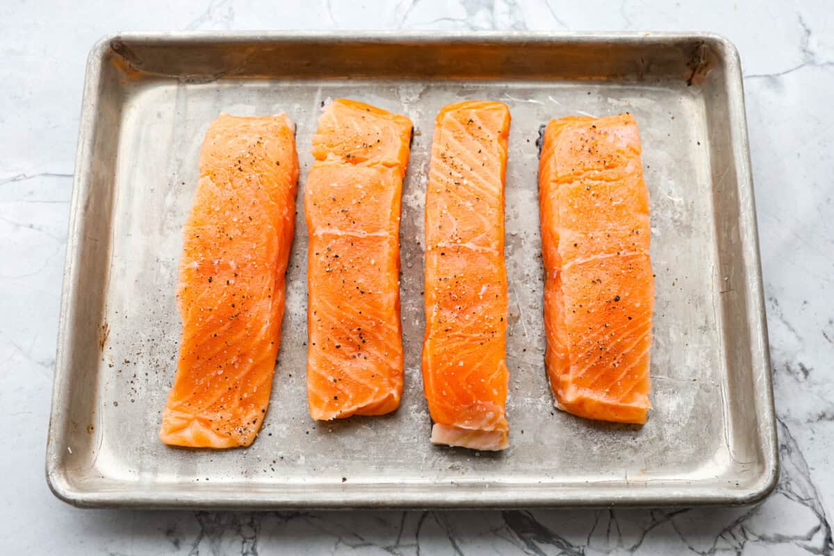 Bang Bang Salmon takes salmon filets, smothers them in bang bang sauce that is sweet with a kick, and then baked to perfection. You will love this simple yet oh-so-tasty dinner that can be ready to serve in less than 30 minutes! Overhead shot of salmon filets on a baking sheet.